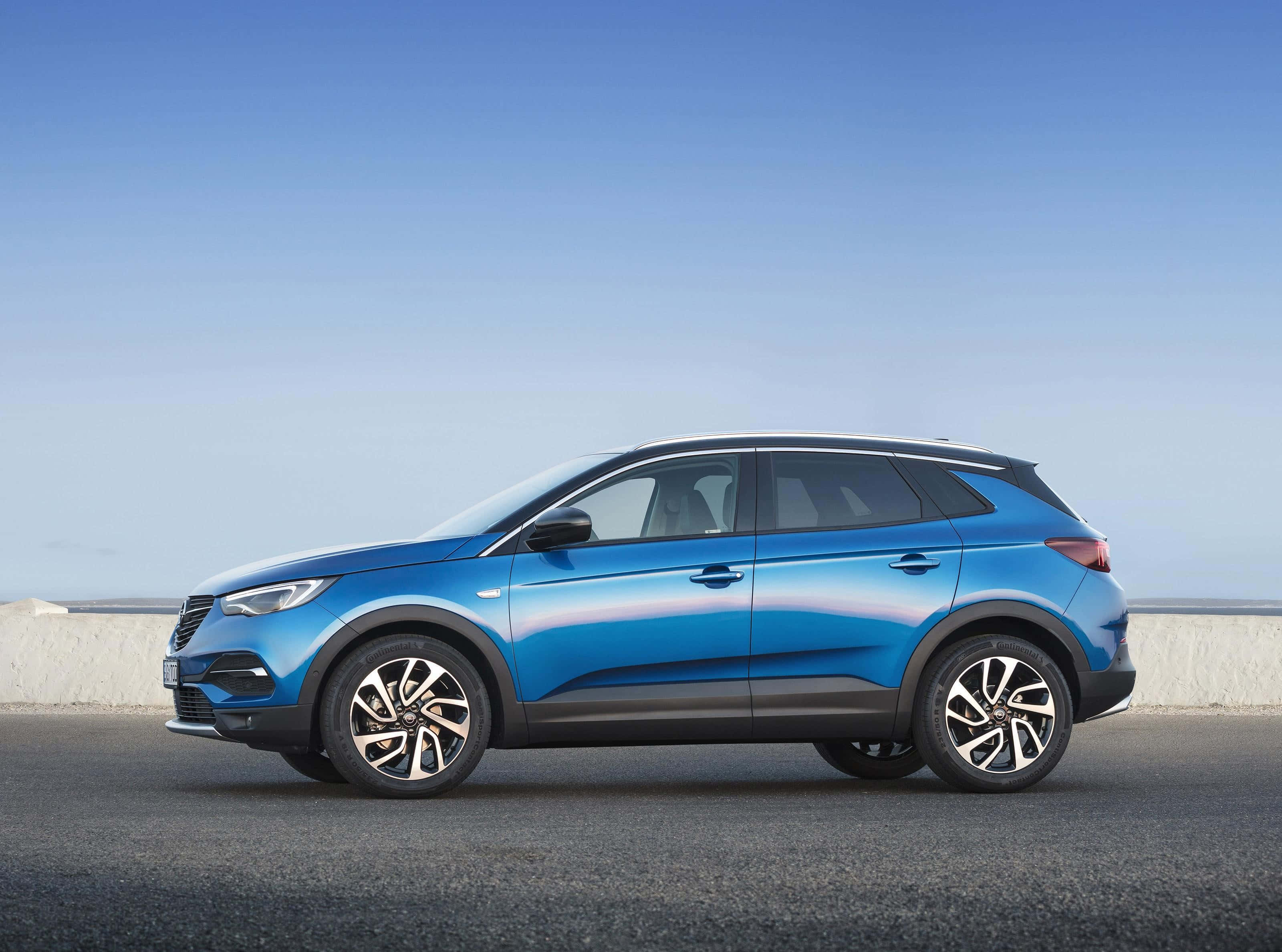 Opel Grandland X 桌布 壁紙 — 一輛時尚的藍色SUV停在沿海公路上，天空晴朗，遠處是海洋。
