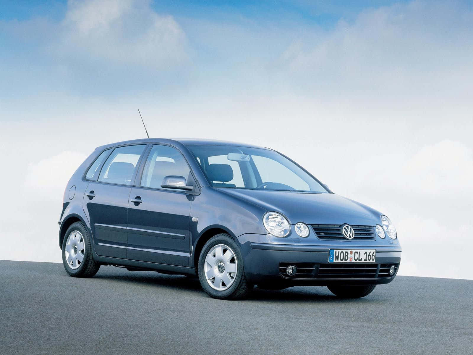 Volkswagen Polo 桌布 壁紙 — 一輛時尚的藍色福斯Polo掀背車停在灰色地面上，天空柔和藍色，帶有縷縷白雲。