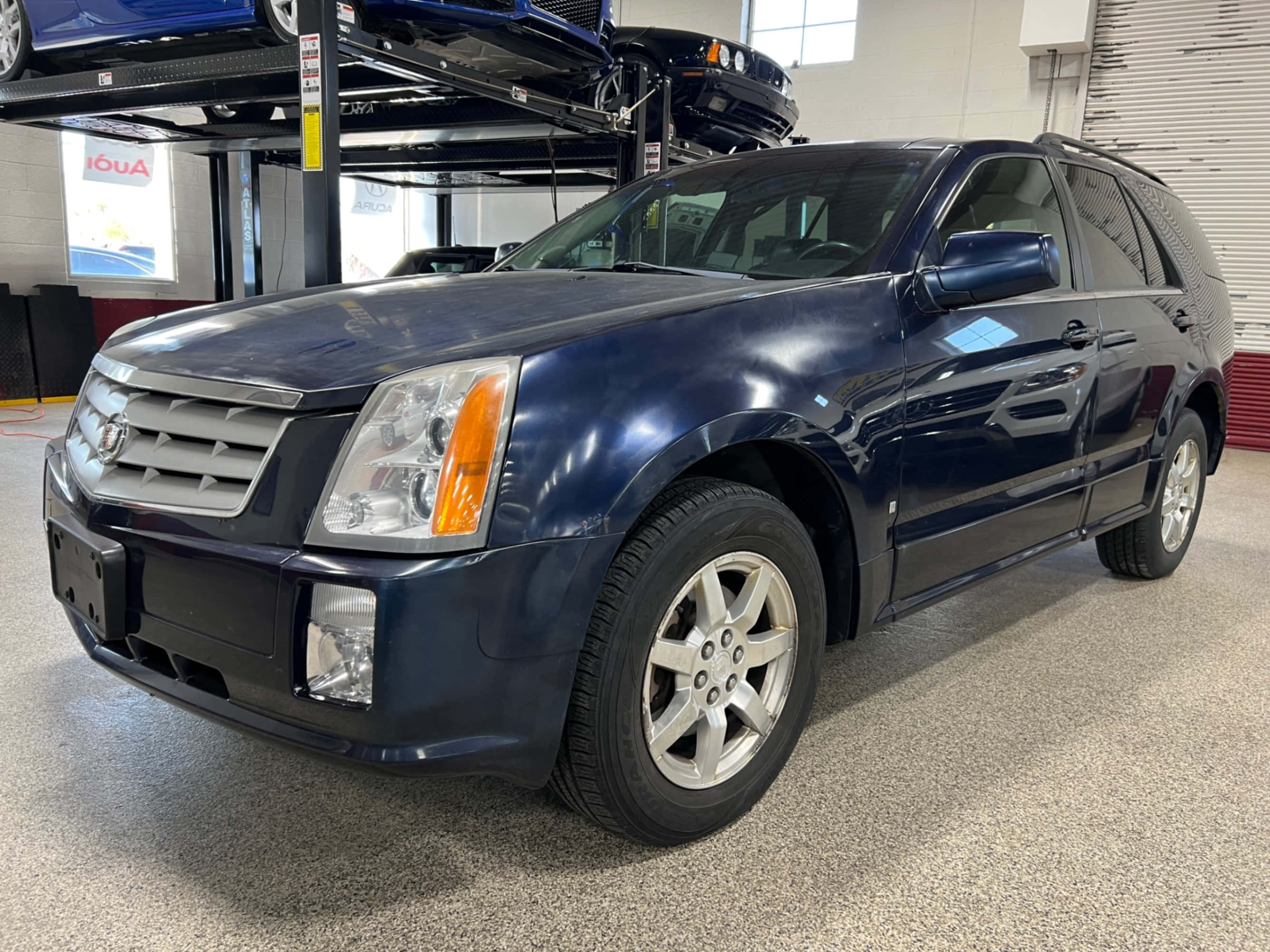 Cadillac Srx 桌布 壁紙 — 一輛時尚的深藍色凱迪拉克SUV在明亮的車庫燈光下閃耀，配備鍍鉻飾件和合金輪圈。