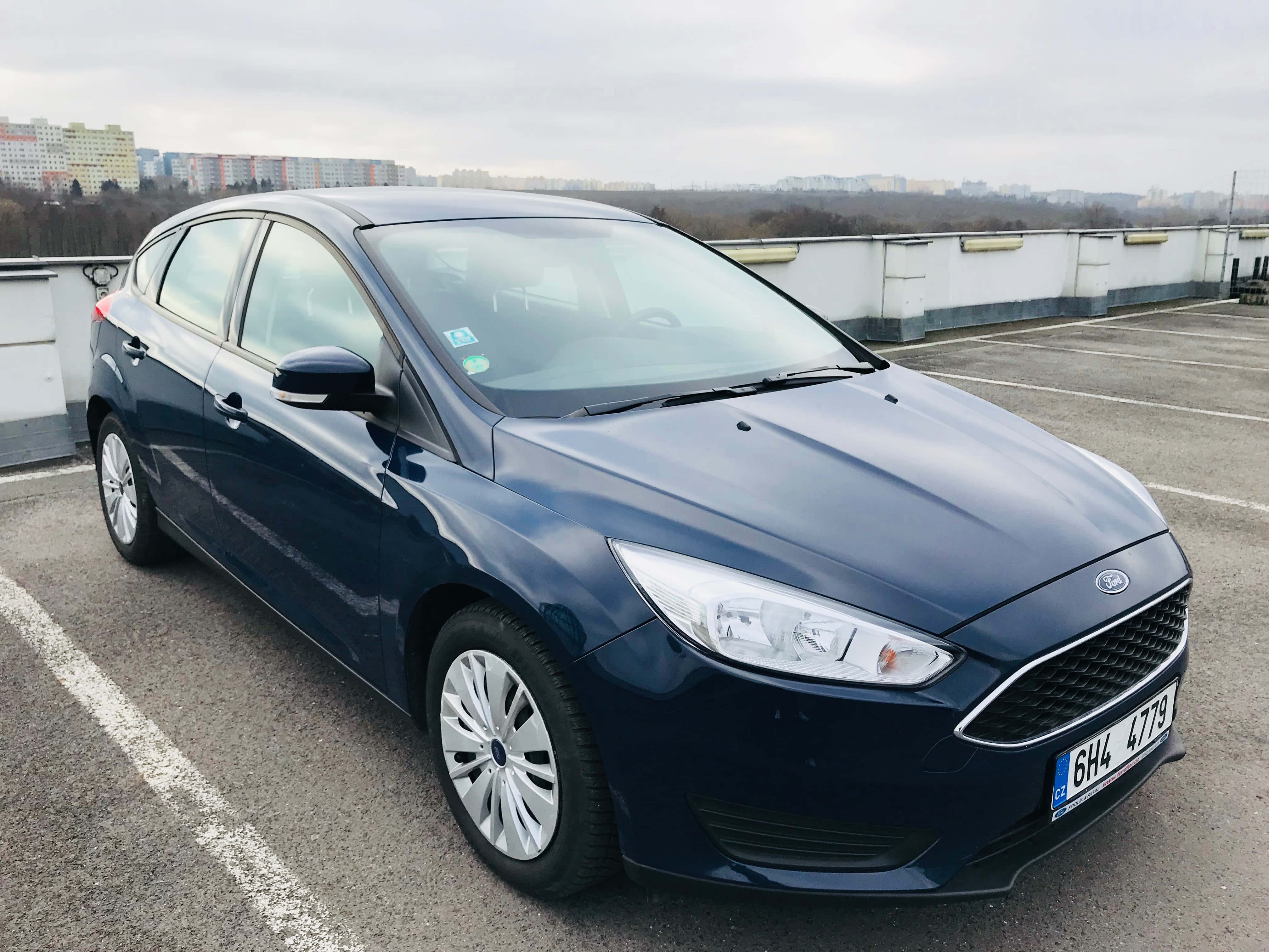 Ford Focus 桌布 壁紙 — 一架時尚的深藍色福特福克斯停放在屋頂停車場，天空多雲，遠處有城市建築。