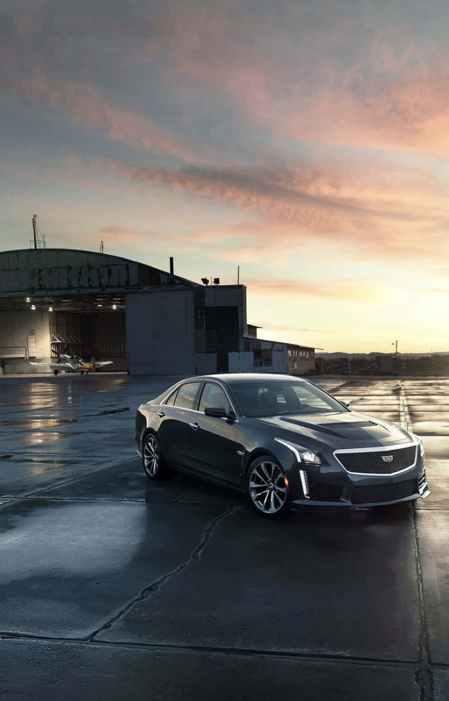 Cadillac Ats 桌布 壁紙 — 一輛時尚的深灰色凱迪拉克CT6停在日落時分的濕滑停機坪上，背景有機庫和飛機。