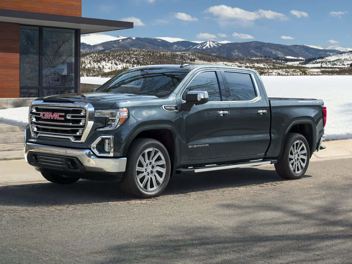 Gmc Sierra 桌布 壁紙 — 一輛時尚的深灰色 GMC Sierra 皮卡車停在鋪滿雪的行車道上，背景是白雪覆蓋的山脈，天空清澈湛藍。