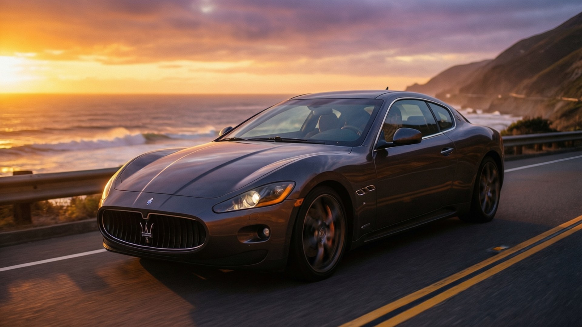 Maserati Granturismo 桌布 壁紙 — 一架時尚的深灰色瑪莎拉蒂跑車沿著海岸公路在日落時分巡航，背後海浪拍打懸崖。