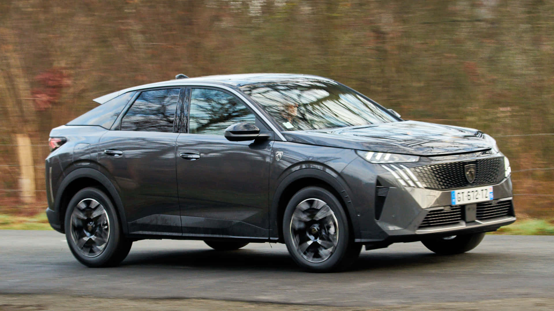  壁紙 — 一輛時尚的深灰色Peugeot SUV沿著道路行駛，背景是模糊的秋樹。