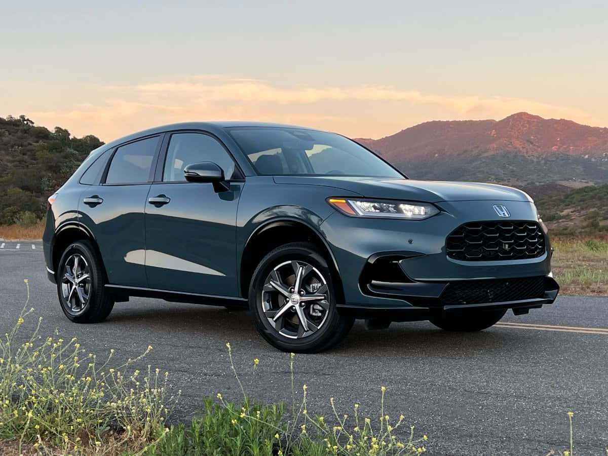 Honda Hr-v 桌布 壁紙 — 一輛時尚的深綠色本田SUV停在路邊，背景是山脈和金色的日落光線。