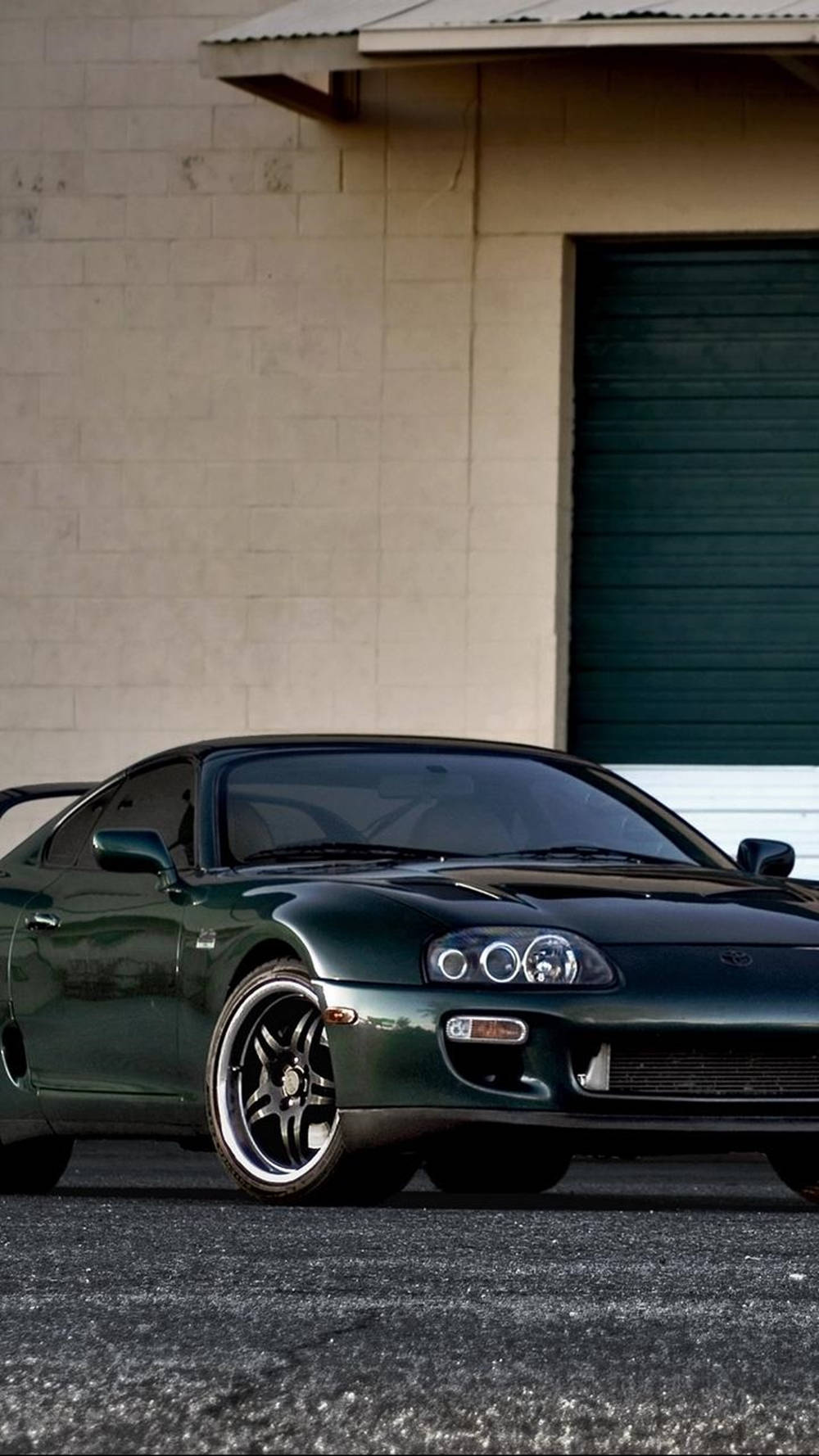深綠色豐田Supra停在帶有綠色車庫門的米色建築前。 — Toyota Supra 壁紙