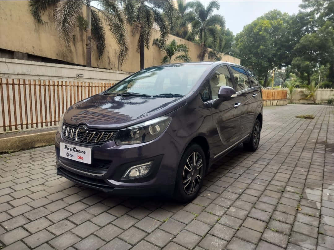 Mahindra Marazzo 桌布 壁紙 — 一架時尚的深紫色緊湊型MPV停放在灰色磚砌車道上，背景有棕櫚樹和米色牆壁。