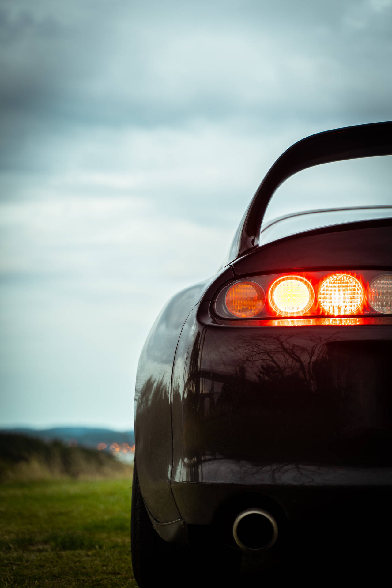 黃昏時停在草地上的黑色跑車，帶有發光的尾燈。 — Toyota Supra 壁紙