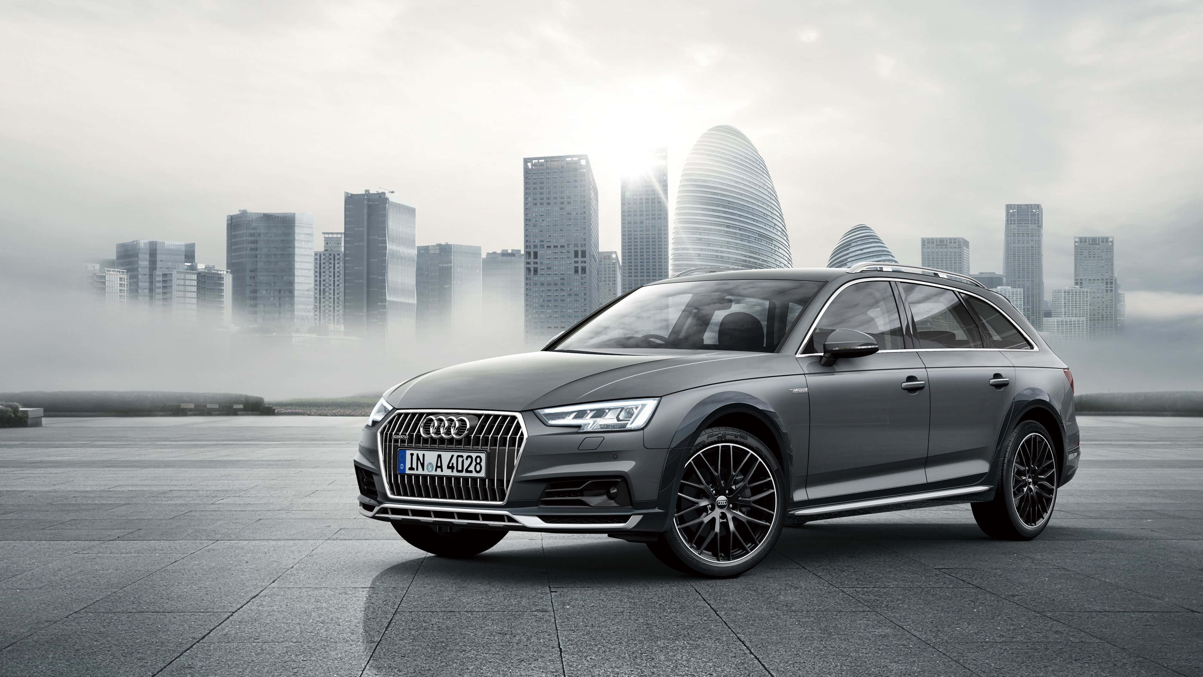 Audi A4 桌布 壁紙 — 一輛時尚的灰色奧迪旅行車停泊在霧氣瀰漫的都市廣場上，現代摩天大樓在柔和的晨光中閃耀。