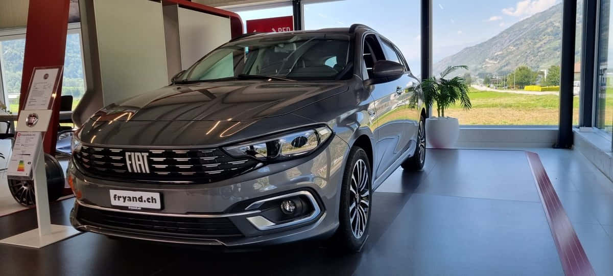 Fiat Tipo 桌布 壁紙 — 一輛時尚的灰色飛雅特轎車在展廳燈光下閃閃發光，透過大窗戶可以看到山脈。