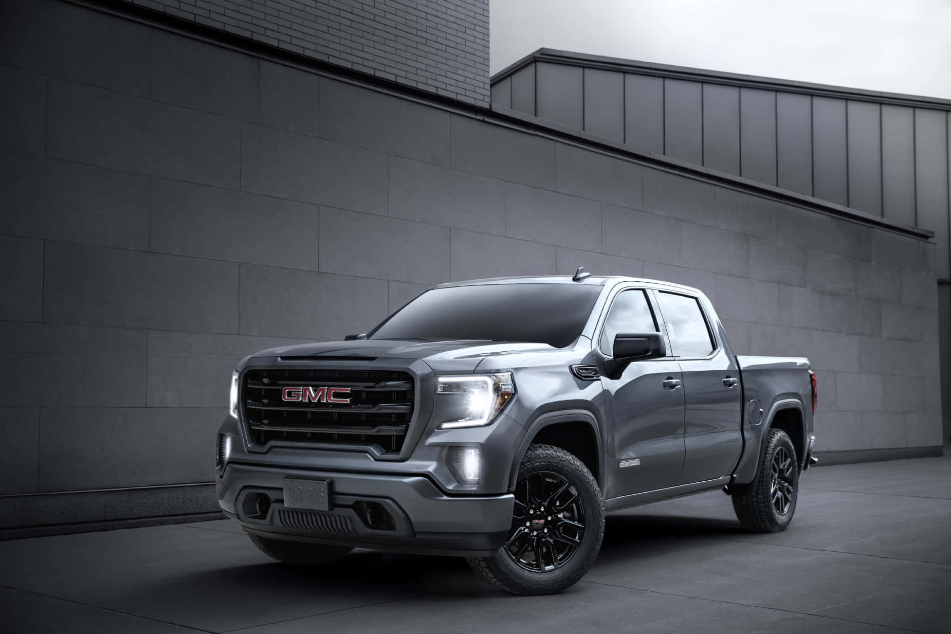 Gmc Sierra 桌布 壁紙 — 一輛時尚的灰色GMC Sierra皮卡車，配備黑色輪圈，停放在現代灰色混凝土牆前，天空多雲。