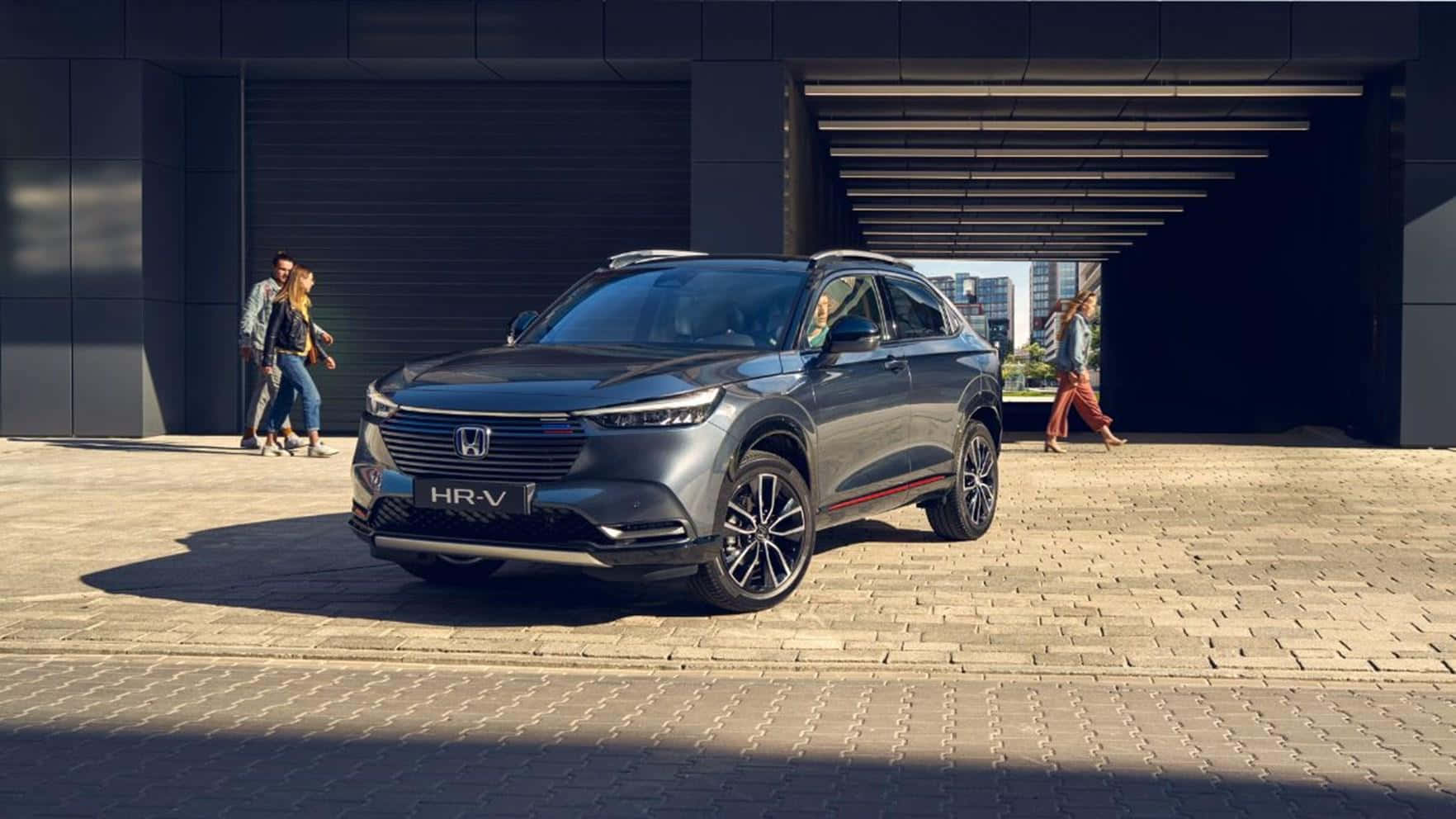 Honda Hr-v 桌布 壁紙 — 一輛時尚的灰色本田HR-V SUV停放在陽光普照的磚砌廣場上，人們在附近的現代建築結構下行走。