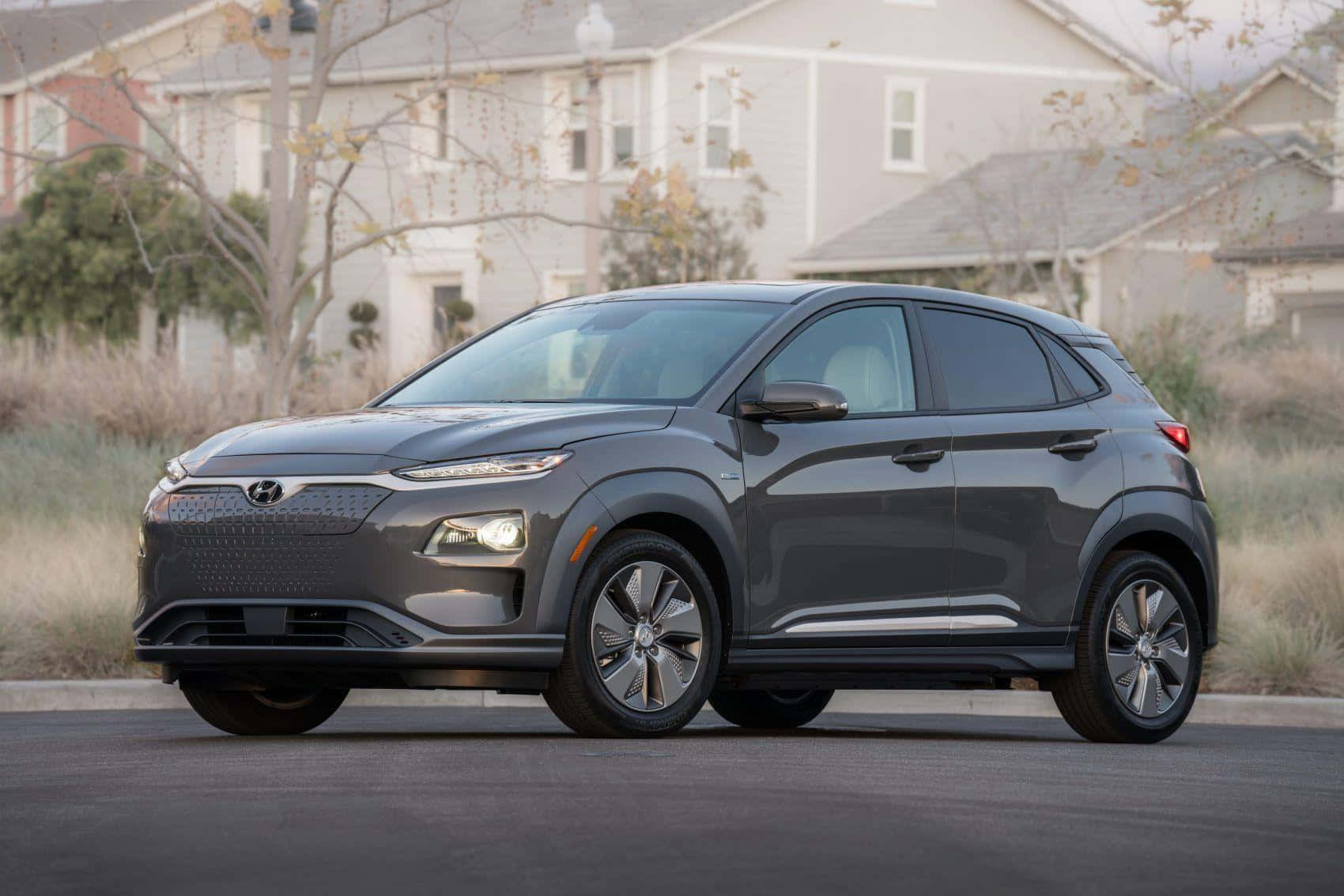 Hyundai Kona 桌布 壁紙 — 一輛時尚灰色Hyundai Kona EV停泊在郊區街道上，背景有房屋和乾草。