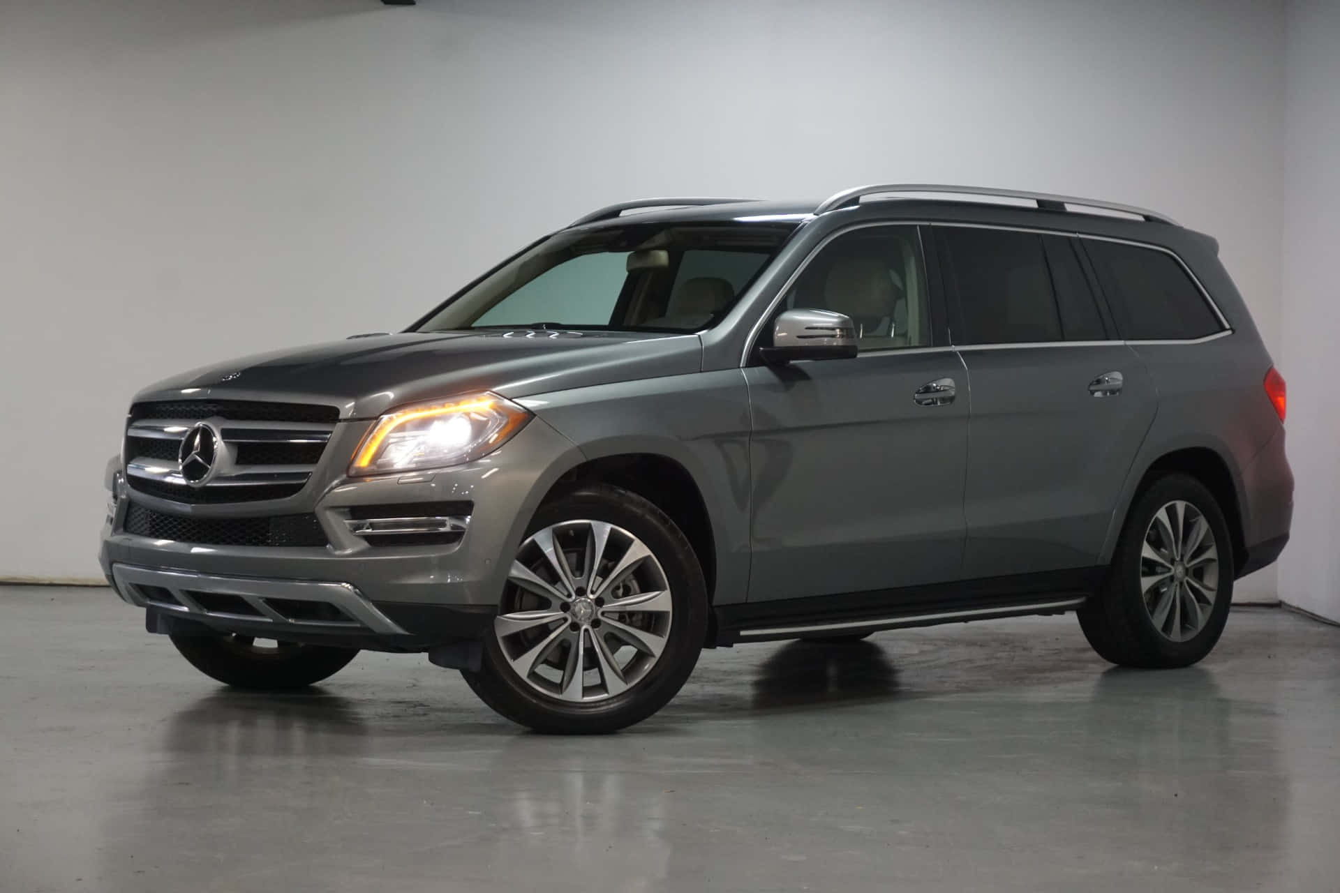 Mercedes-benz Gl-class 桌布 壁紙 — 一輛時尚的灰色Mercedes-Benz GL-Class SUV在極簡主義工作室中展示，配有反射地板和柔和燈光。