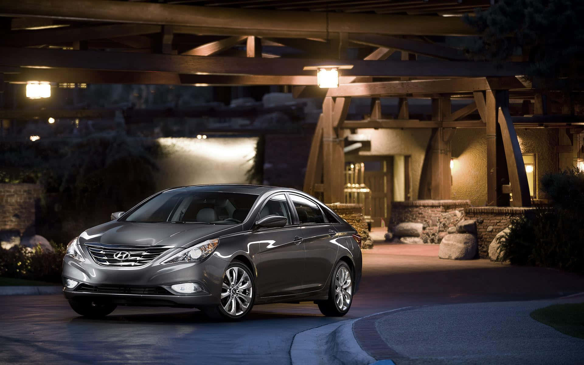 Hyundai Sonata 桌布 壁紙 — 一輛時尚的灰色轎車在夜間停放在木製涼亭下，溫暖的燈光照亮其拋光表面。