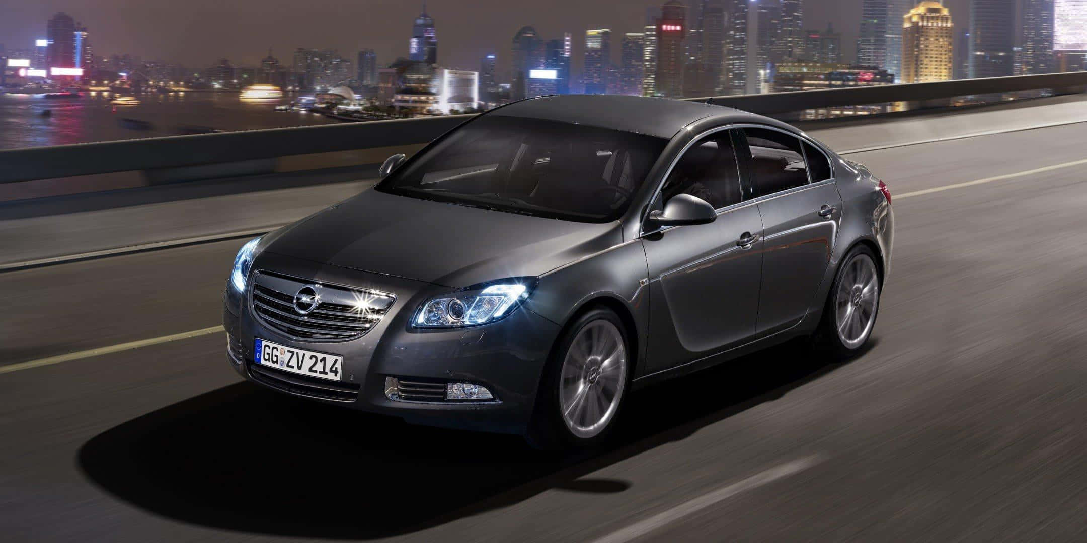 Opel Insignia 桌布 壁紙 — 一輛時尚灰色房車在夜間高速駛過橋樑，背景是閃爍的活力城市天際線。