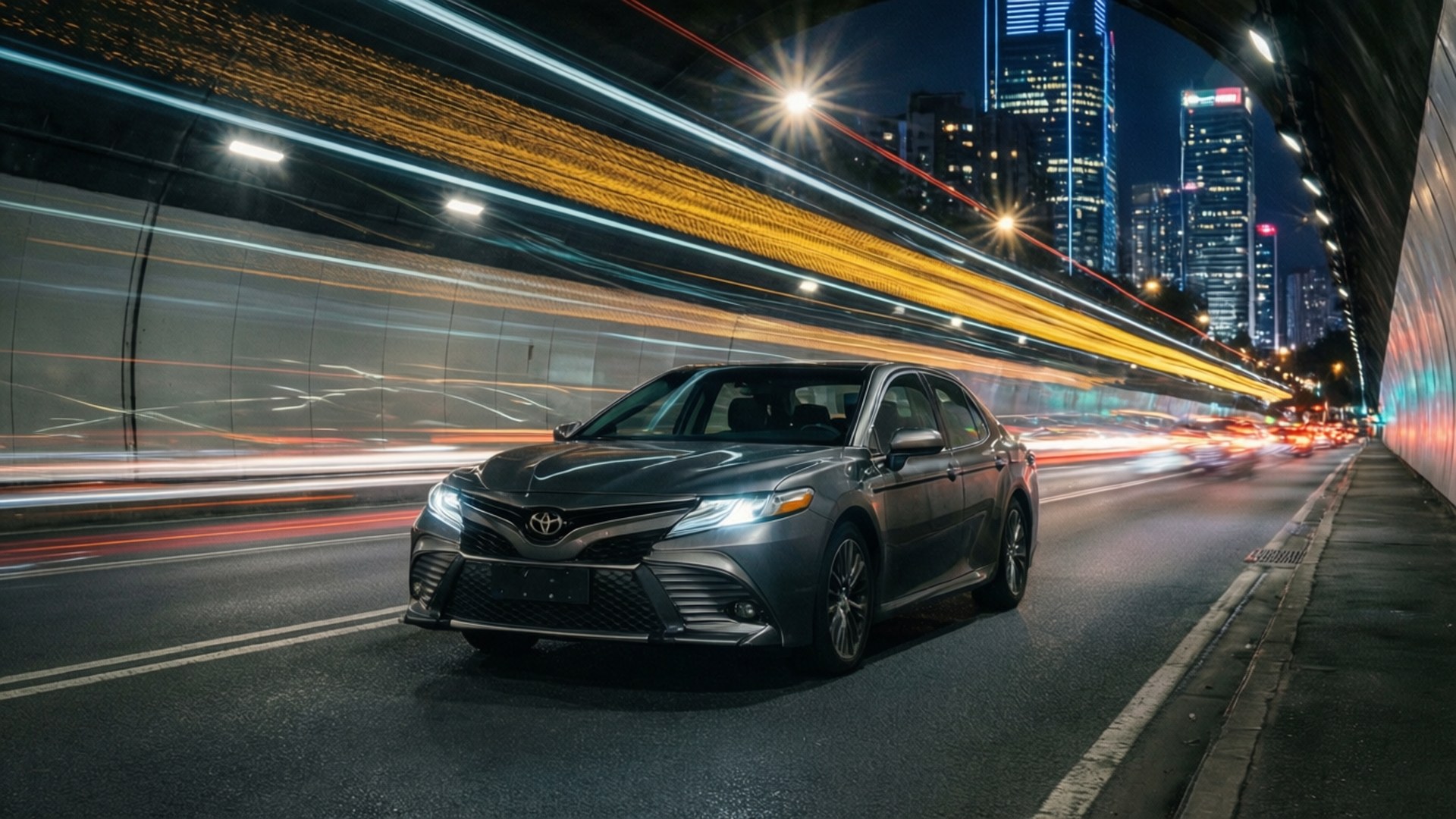 Camry Light Tunnel 壁紙 — 一輛時尚的灰色轎車在夜間高速穿過隧道，城市燈光形成鮮豔的黃色和紅色條紋模糊掠過。