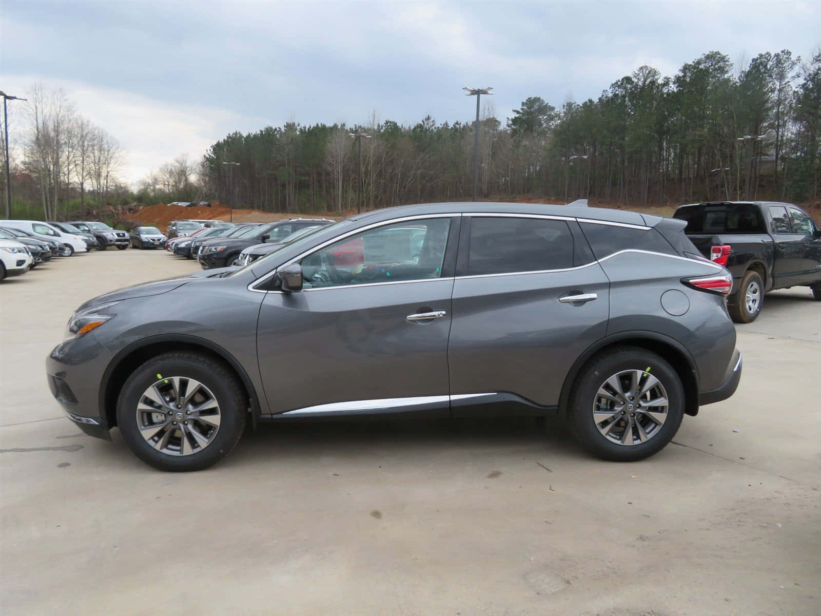Nissan Murano 桌布 壁紙 — 一輛時尚的灰色SUV停放在一個有樹木和其他車輛的停車場，天空多雲。