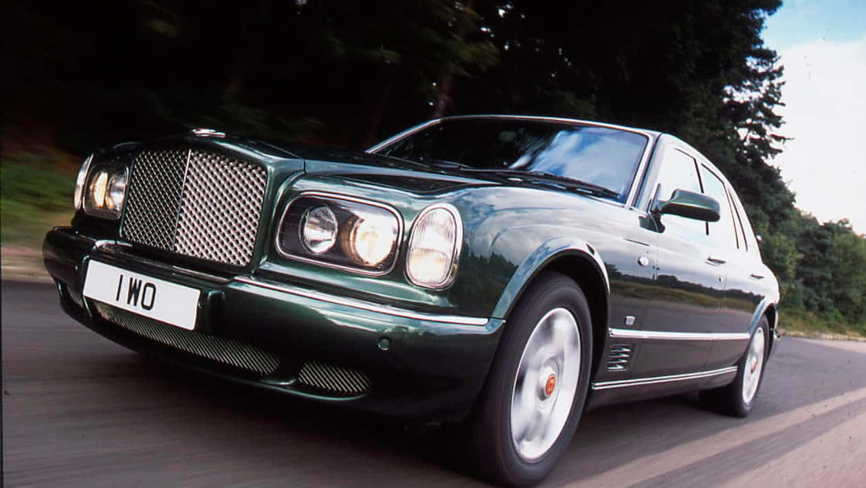 Bentley Arnage 桌布 壁紙 — 一輛時尚的綠色賓利 Arnage 在綠樹成蔭的道路上奔馳，動態模糊效果凸顯其奢華與動力。