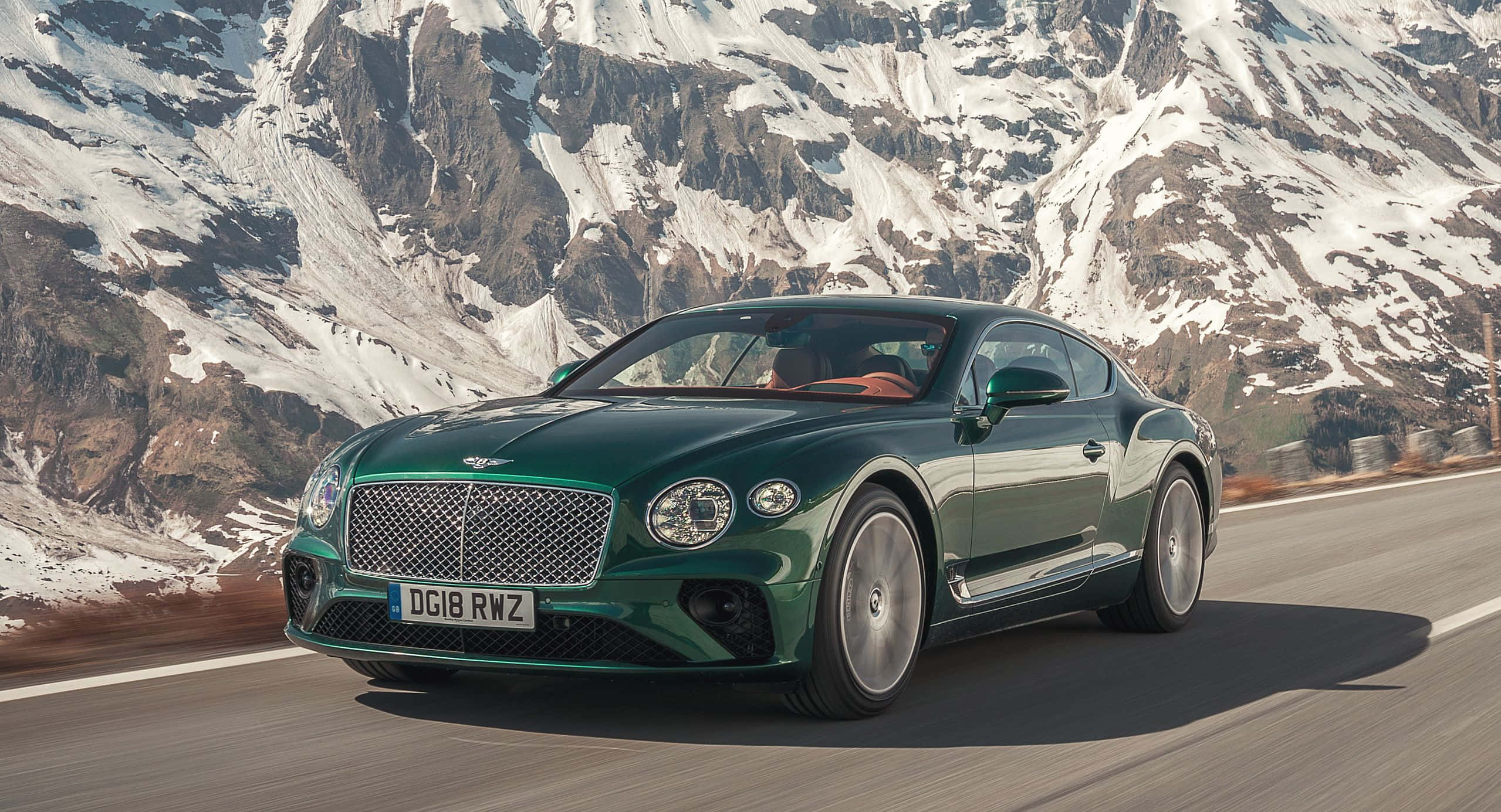 Bentley Continental Gt 桌布 壁紙 — 一輛時尚的綠色賓利 Continental GT 沿著蜿蜒的山路行駛，背景是白雪覆蓋的山峰。
