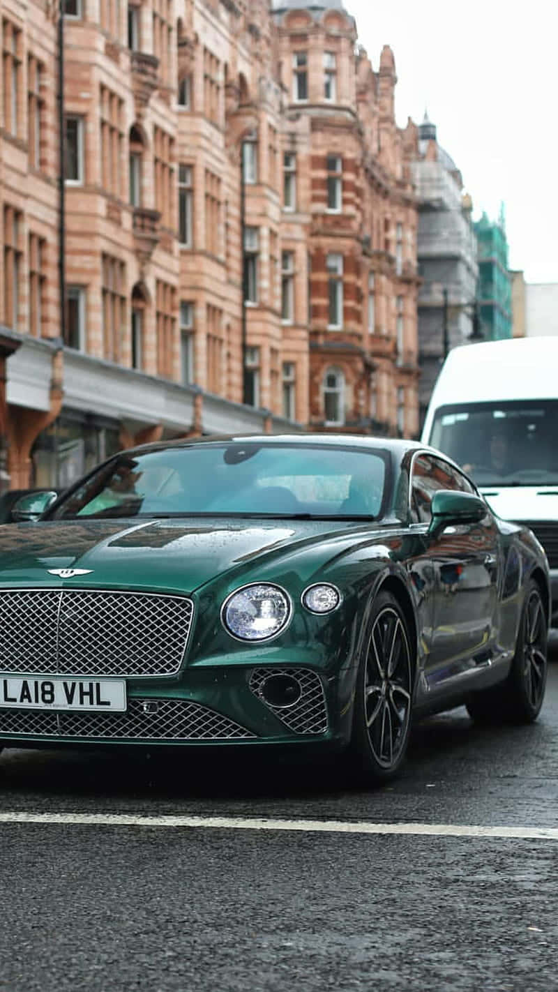 Bentley Continental Gt 桌布 壁紙 — 一輛時尚的綠色賓利 Continental GT 停在潮濕的城市街道上，旁邊是華麗的磚造建築。