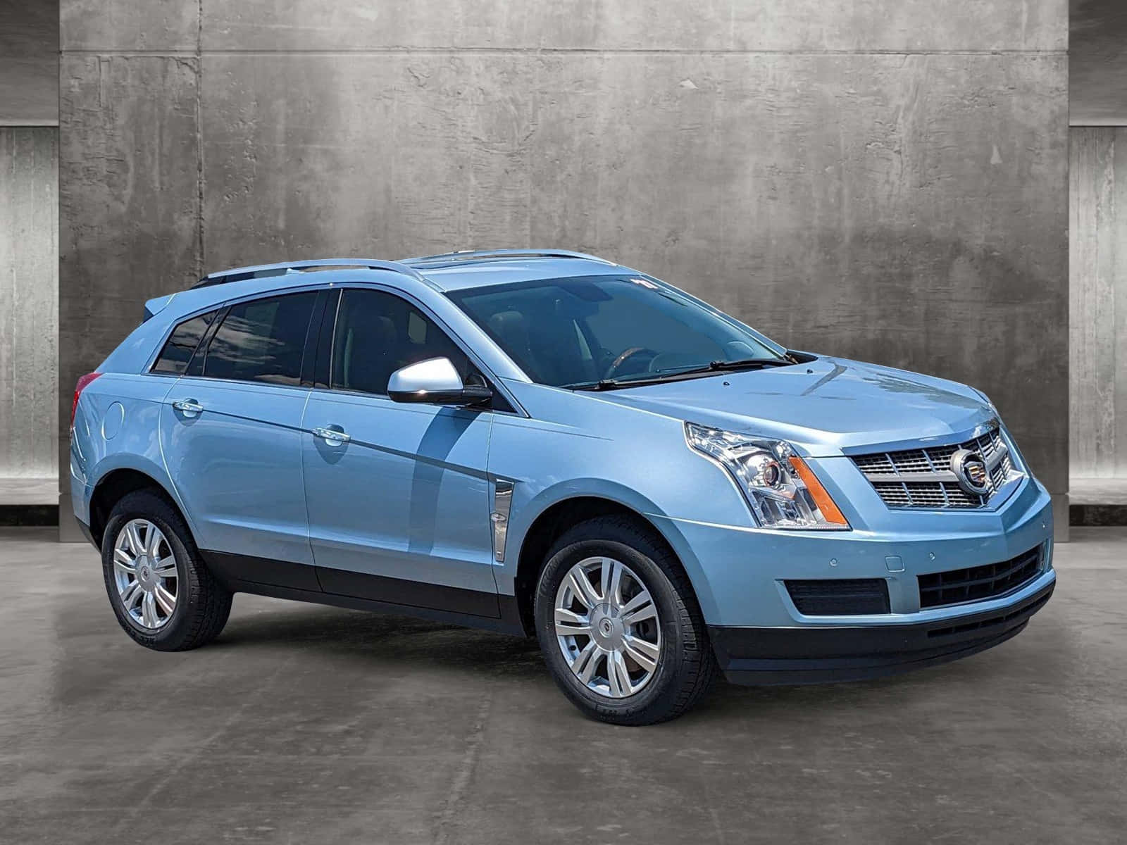 Cadillac Srx 桌布 壁紙 — 一輛時尚的淺藍色 Cadillac SRX SUV 停放在質感灰色混凝土牆前，處於極簡主義工作室環境中。