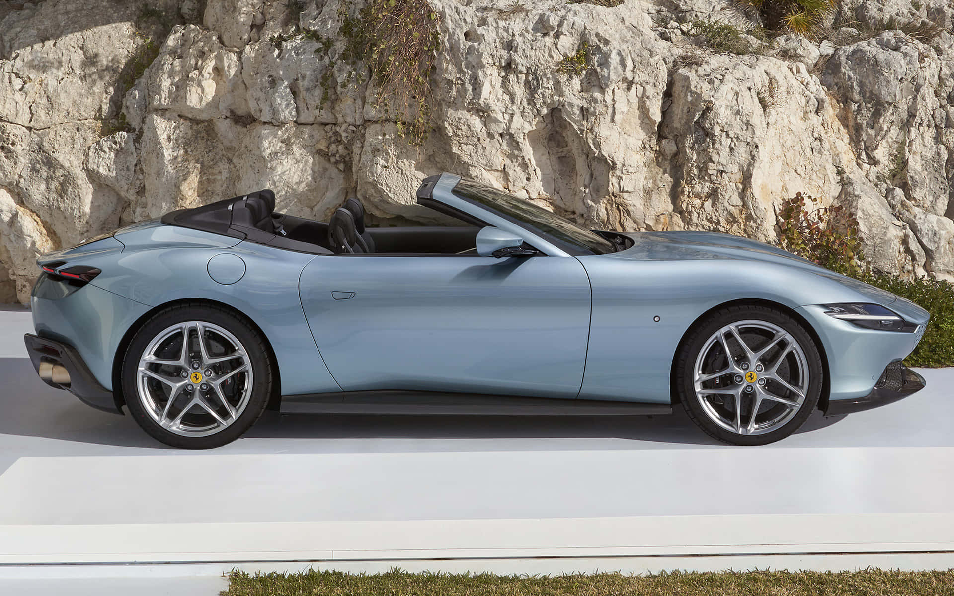 Ferrari Roma 桌布 壁紙 — 一架時尚的淺藍色法拉利敞篷車停放在白色平台上，背景是崎嶇的岩石懸崖。