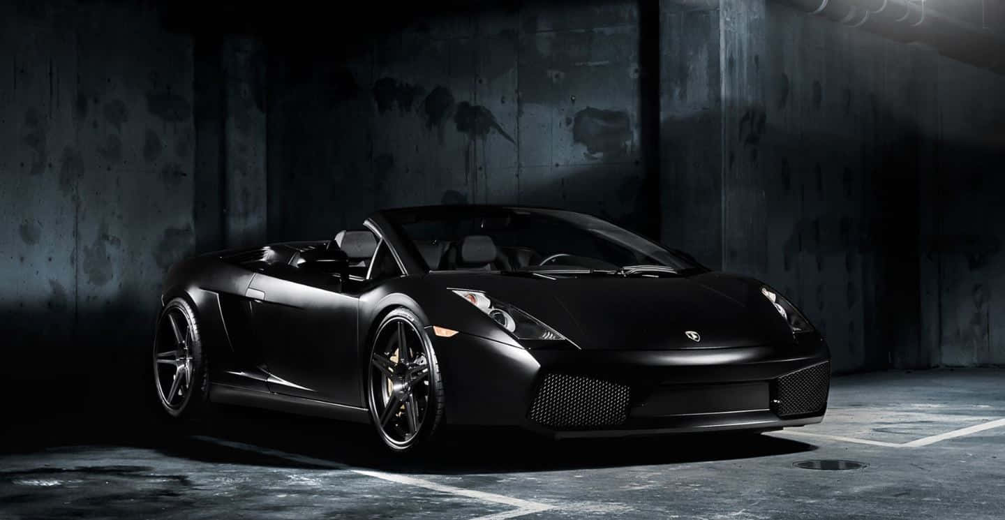 Lamborghini Gallardo 桌布 壁紙 — 一架時尚啞黑色藍寶堅尼Gallardo Spyder停放在燈光昏暗的混凝土車庫中，搭配戲劇性的聚光燈照明。