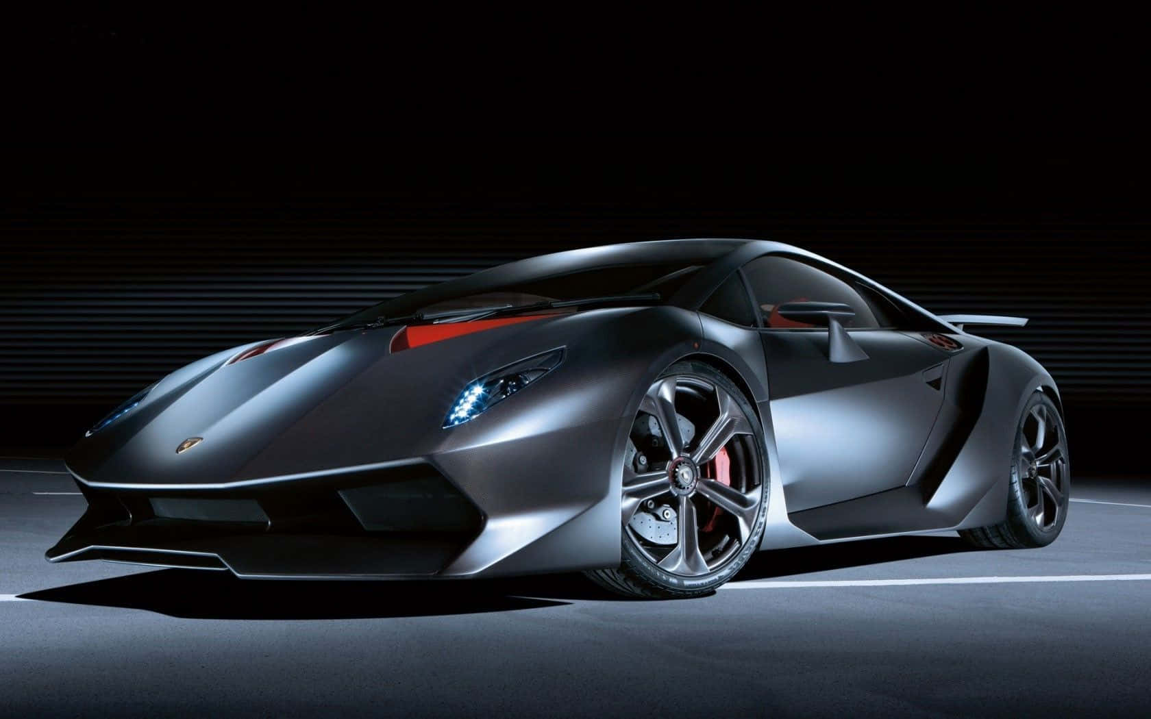 Lamborghini Sesto Elemento 桌布 壁紙 — 一輛時尚的啞光黑色藍寶堅尼跑車，帶有發光的藍色車頭燈和紅色點綴，在黑暗的攝影棚背景下戲劇性地照亮。