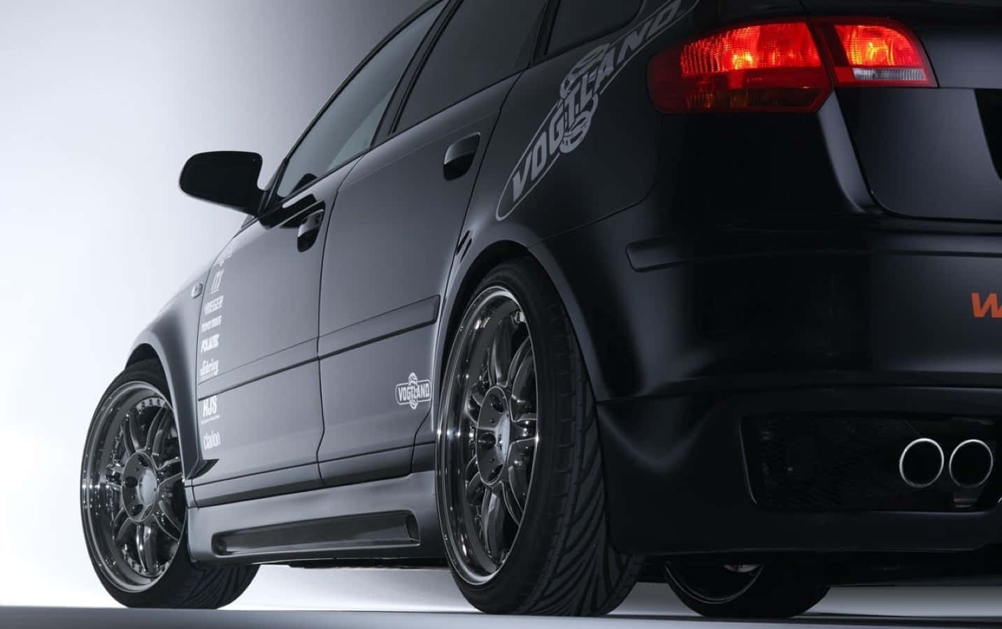 Audi A3 桌布 壁紙 — 一輛時尚的啞光黑色改裝轎車，配備定制輪圈和雙排氣管，在攝影棚燈光下閃耀。