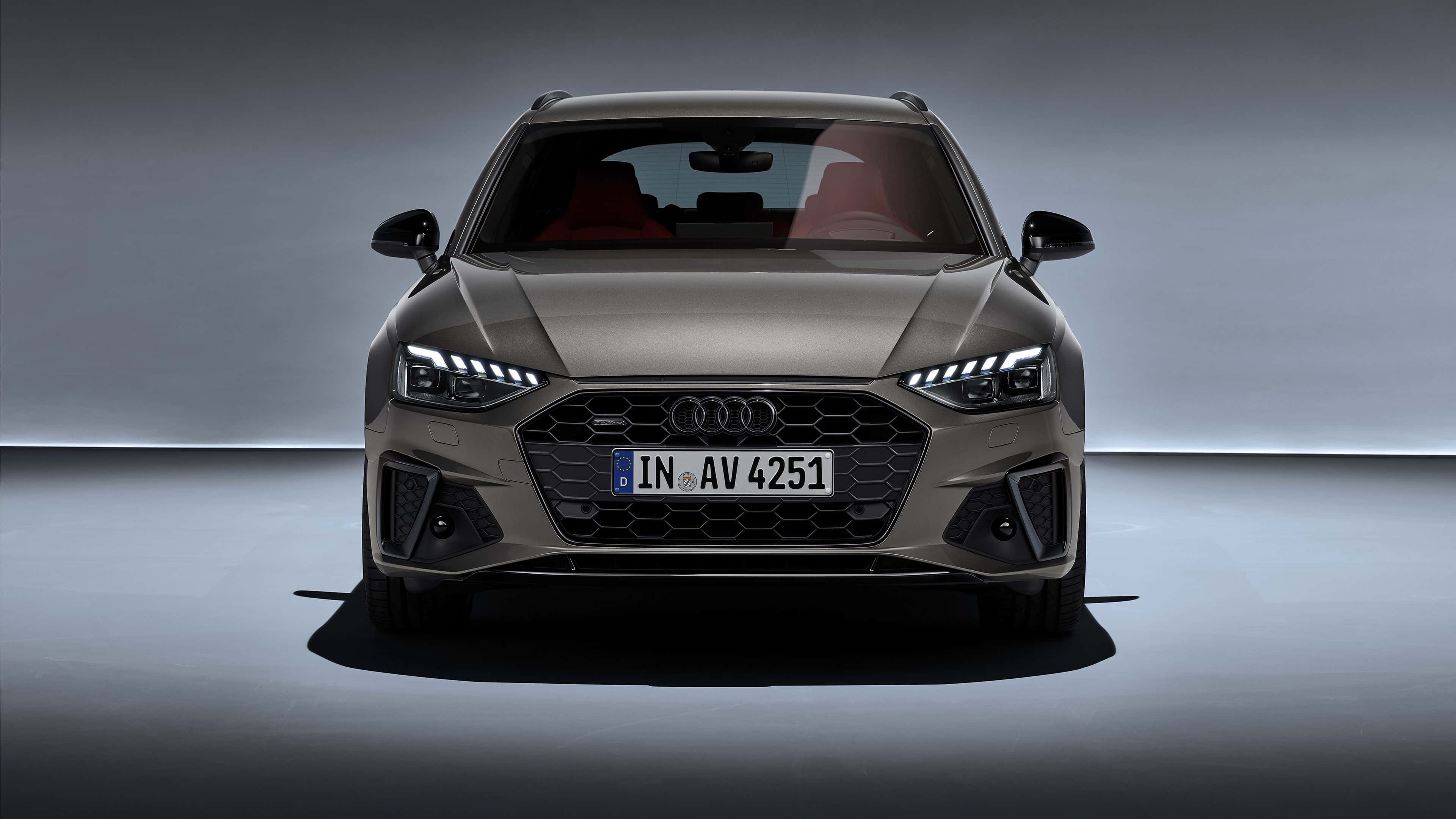Audi A4 桌布 壁紙 — 一輛時尚的啞光灰色奧迪旅行車在簡約的工作室中正面朝前，帶有戲劇性的燈光和紅色內飾點綴。