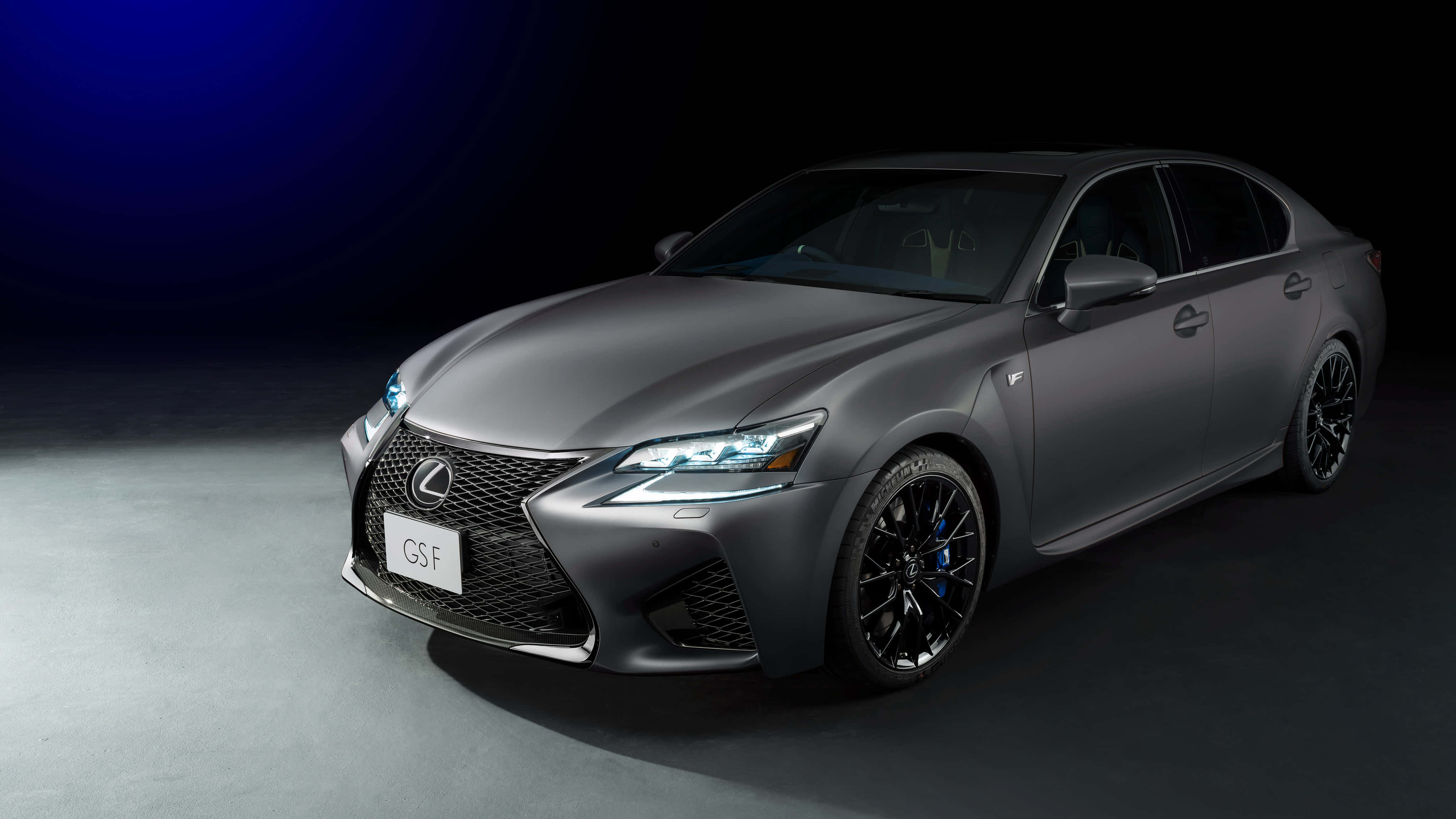 Lexus Gs F 桌布 壁紙 — 一輛時尚的啞光灰色雷克薩斯GS F運動轎車在攝影棚燈光下，在深藍色漸變背景前閃耀。