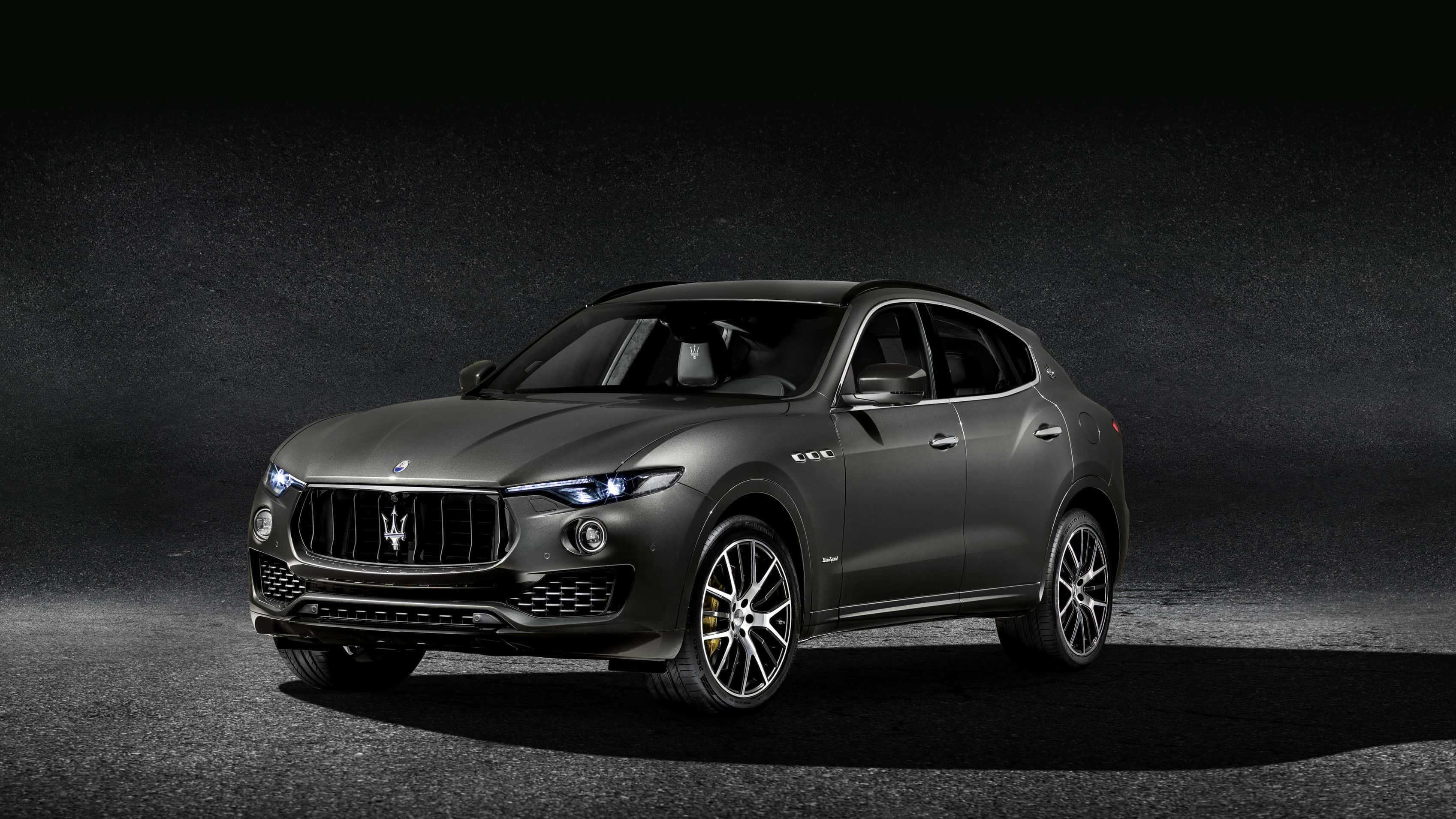 Maserati Levante 桌布 壁紙 — 一輛時尚的啞光灰色瑪莎拉蒂 Levante SUV 在戲劇性的工作室燈光下，在深色紋理背景上閃耀。