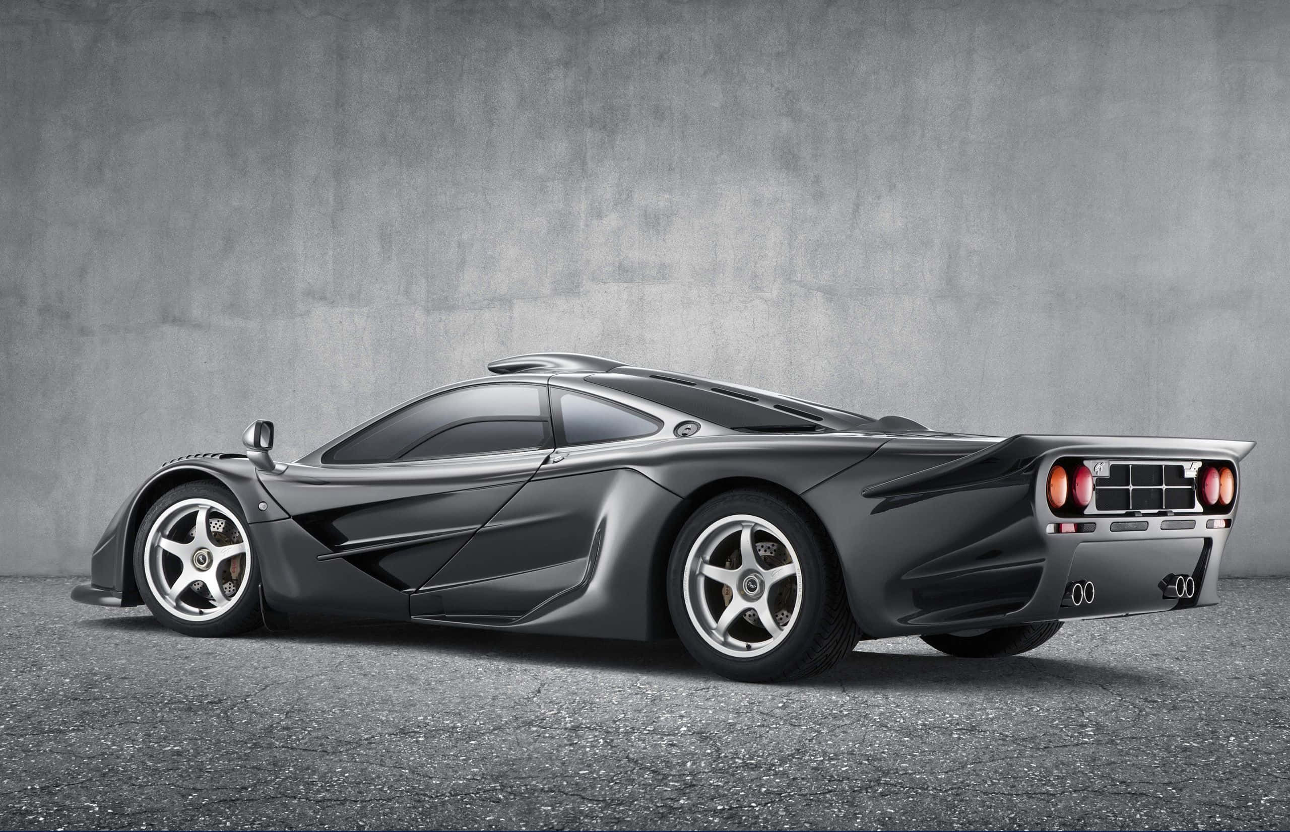 Mclaren F1 桌布 壁紙 — 一輛時尚的啞光灰色McLaren F1超級跑車以側面輪廓展示，背景是帶紋理的混凝土牆壁和地板。