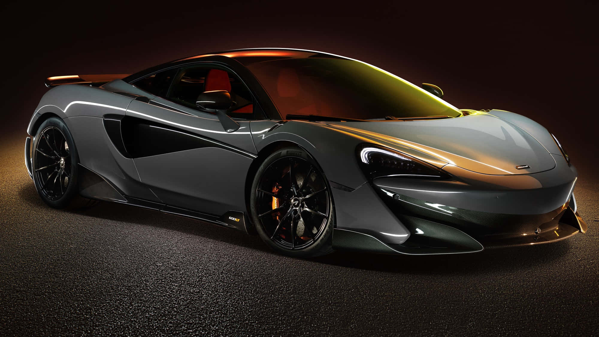 Mclaren 600lt 桌布 壁紙 — 一輛時尚的啞光灰色McLaren跑車在黑暗的工作室背景下，在戲劇性的金色燈光下閃閃發光。