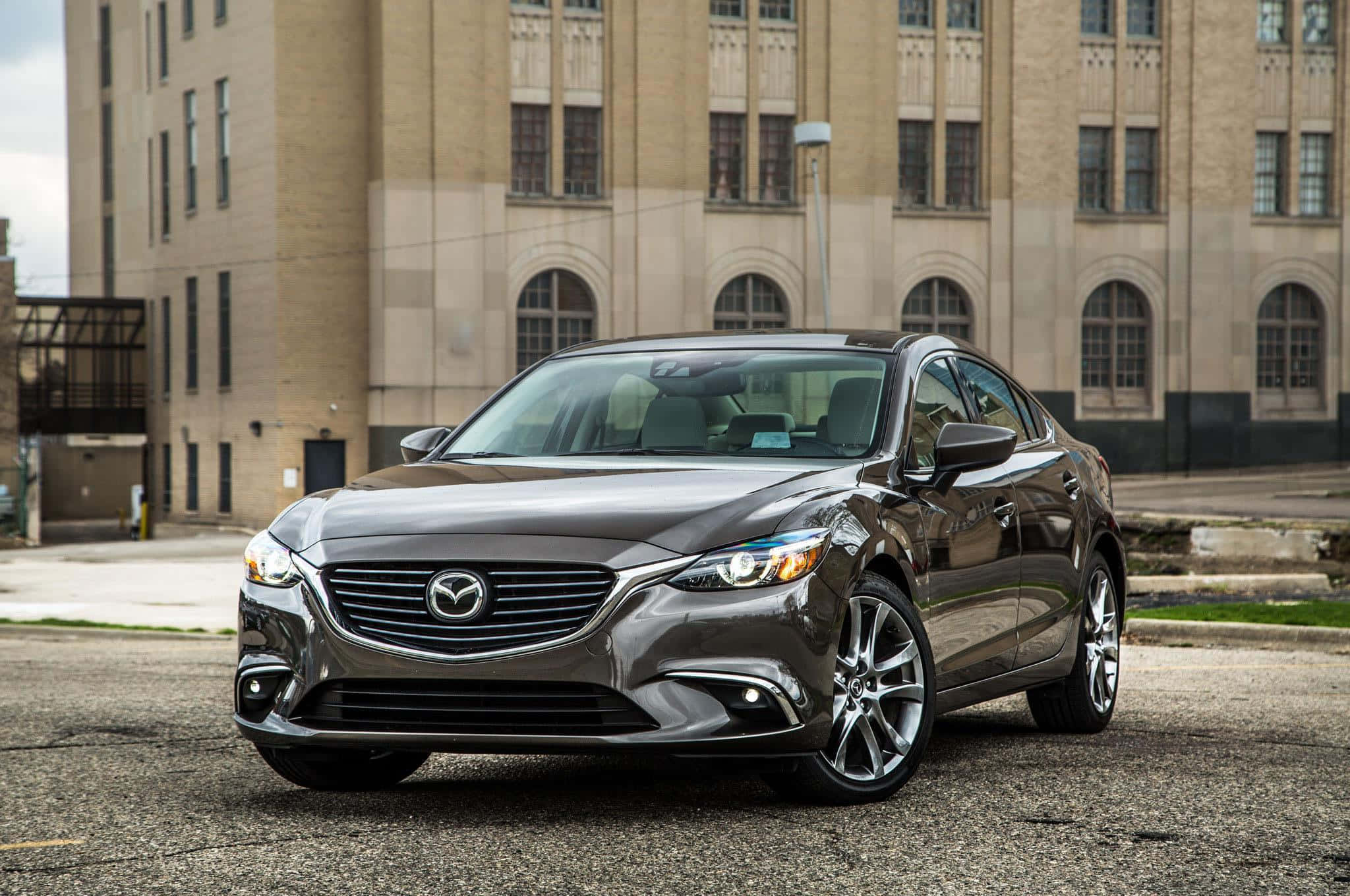 Mazda 6 桌布 壁紙 — 一輛時尚的金屬灰馬自達轎車停在柏油路上，背景是米色磚造建築。