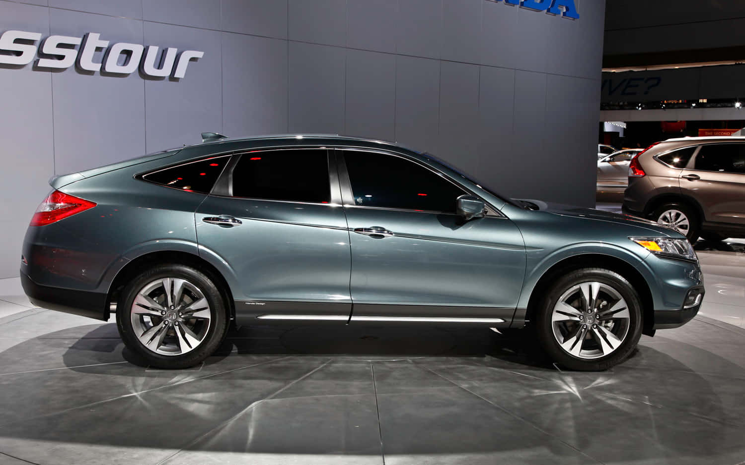 Honda Crosstour 桌布 壁紙 — 一輛時尚金屬青綠色的本田Crosstour轎車在車展上展示，地面光滑，燈光明亮，背景帶有品牌標誌。