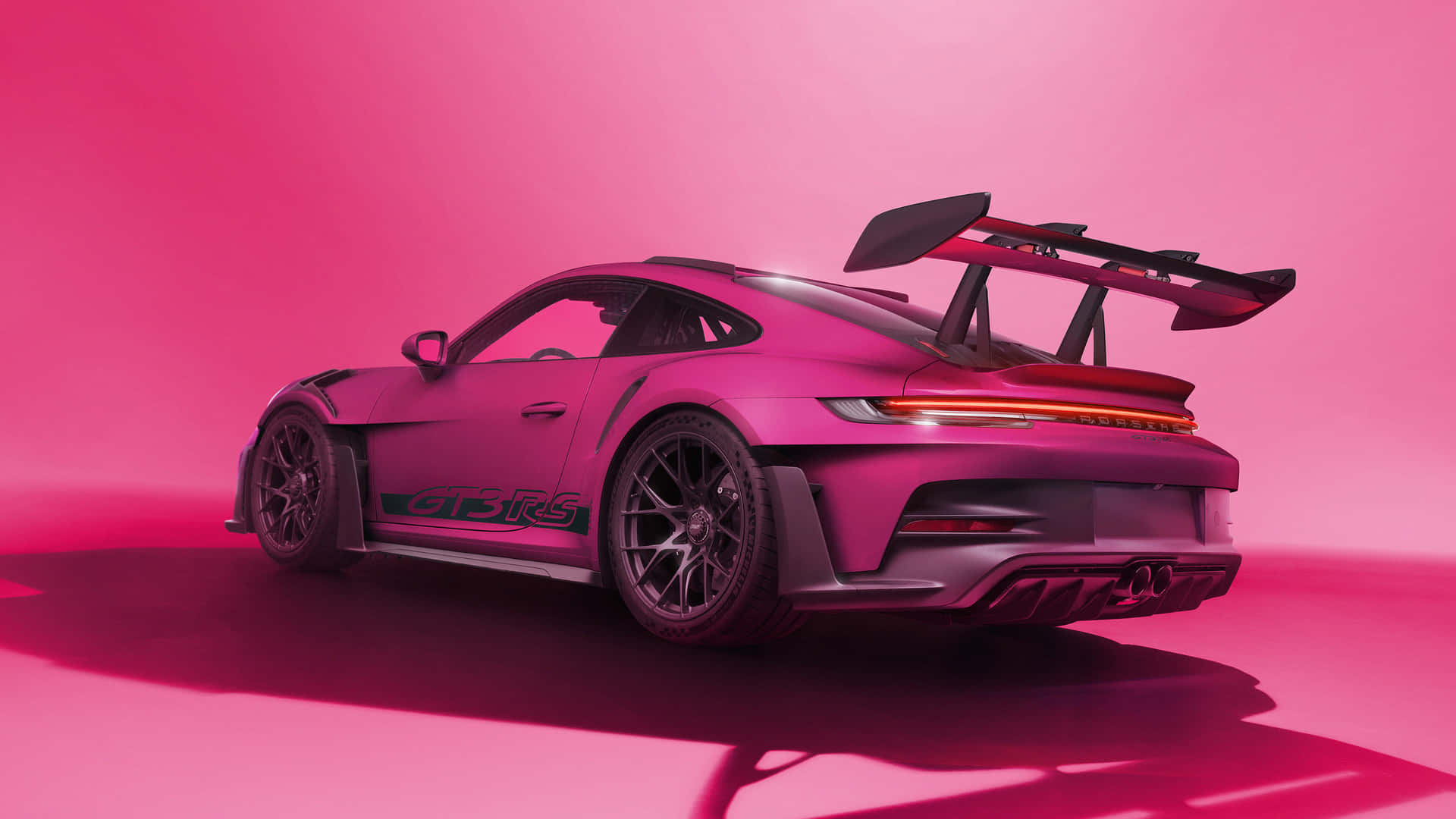  壁紙 — 一輛時尚的粉紅色保時捷911 GT3 RS跑車，配備大型後擾流板，在充滿活力的粉紅色攝影棚背景下展示。