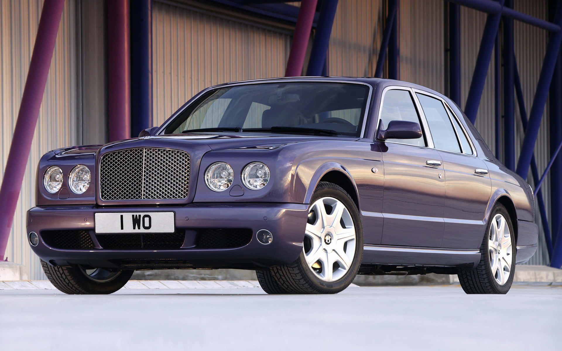 Bentley Arnage 桌布 壁紙 — 一輛時尚的紫色賓利轎車在明亮燈光下閃耀，背景是現代工業風格，帶有紫色和藍色的結構樑。