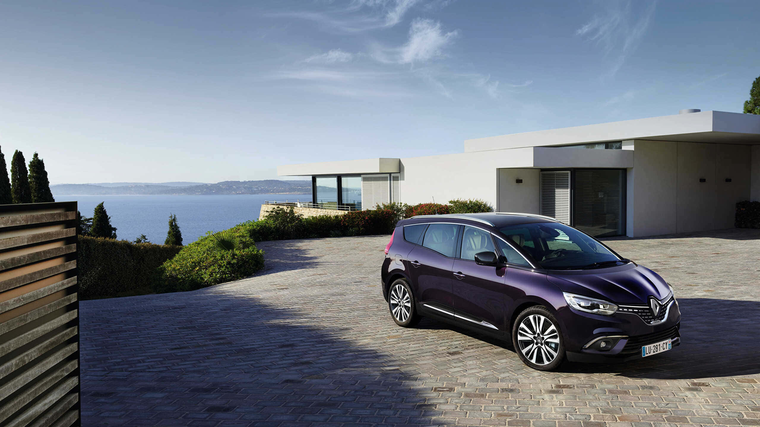 Renault Scenic 桌布 壁紙 — 一架流線型紫色雷諾Scenic停放在石頭車道上，旁邊是一座現代白色房屋，俯瞰著晴朗天空下的廣闊藍色大海。