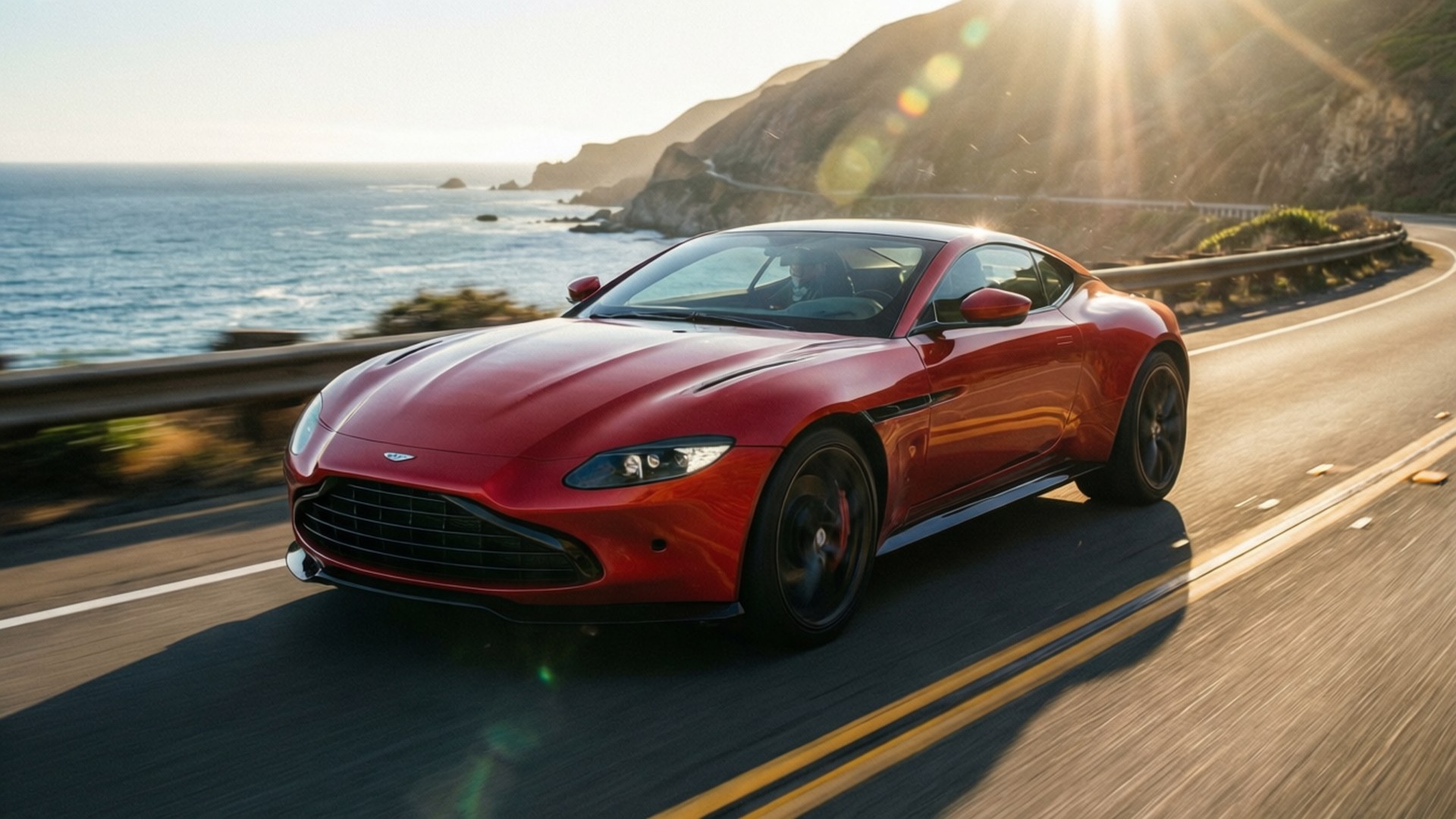 Coastal Speed V8 壁紙 — 一輛流線型的紅色Aston Martin沿著海岸公路飛馳，背景是海洋懸崖和太陽耀斑。