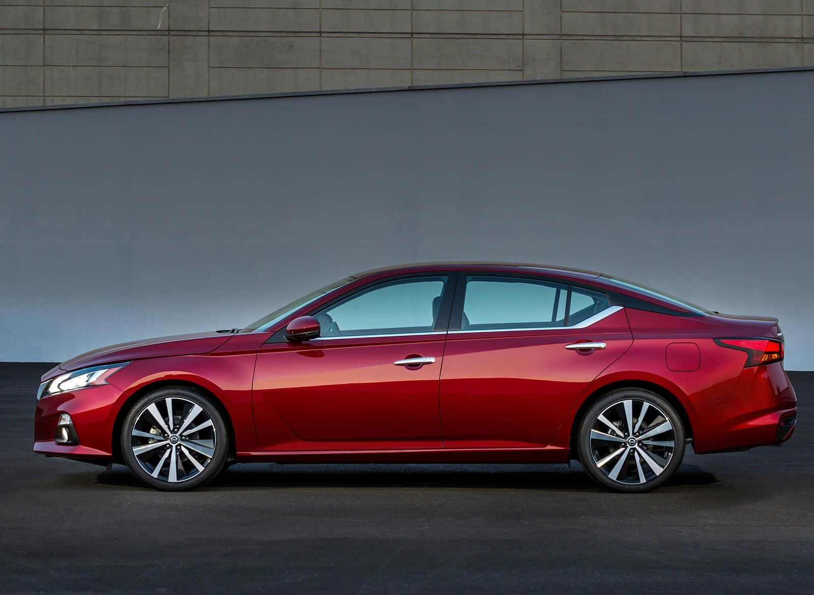 Nissan Altima 桌布 壁紙 — 一輛時尚的紅色轎車在攝影棚燈光下閃閃發光，背景是簡約的混凝土和灰色牆壁。