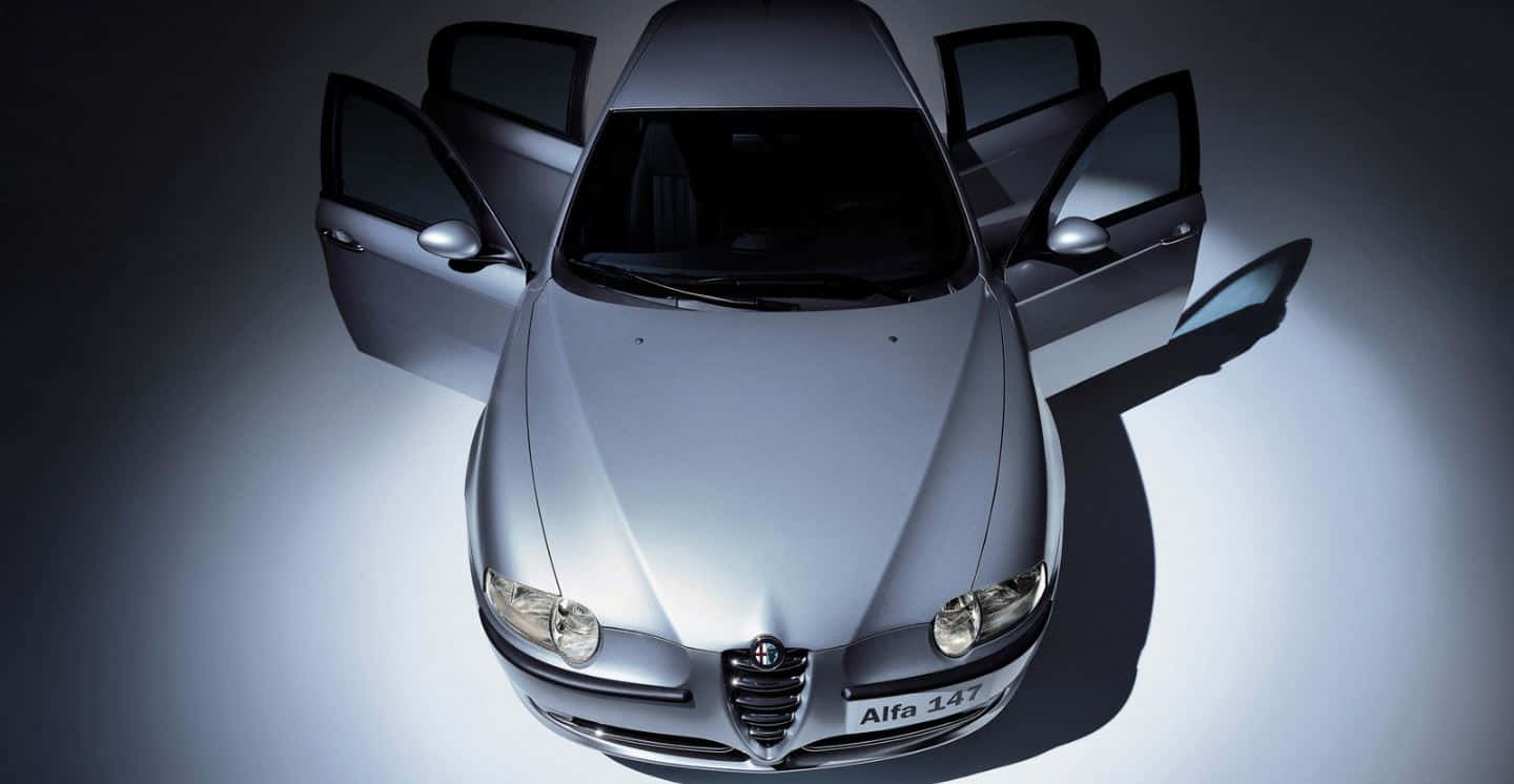 Alfa Romeo 147 桌布 壁紙 — 從上方俯瞰一輛時尚的銀色愛快147跑車，所有車門打開，背景為聚光燈照射的黑暗背景。