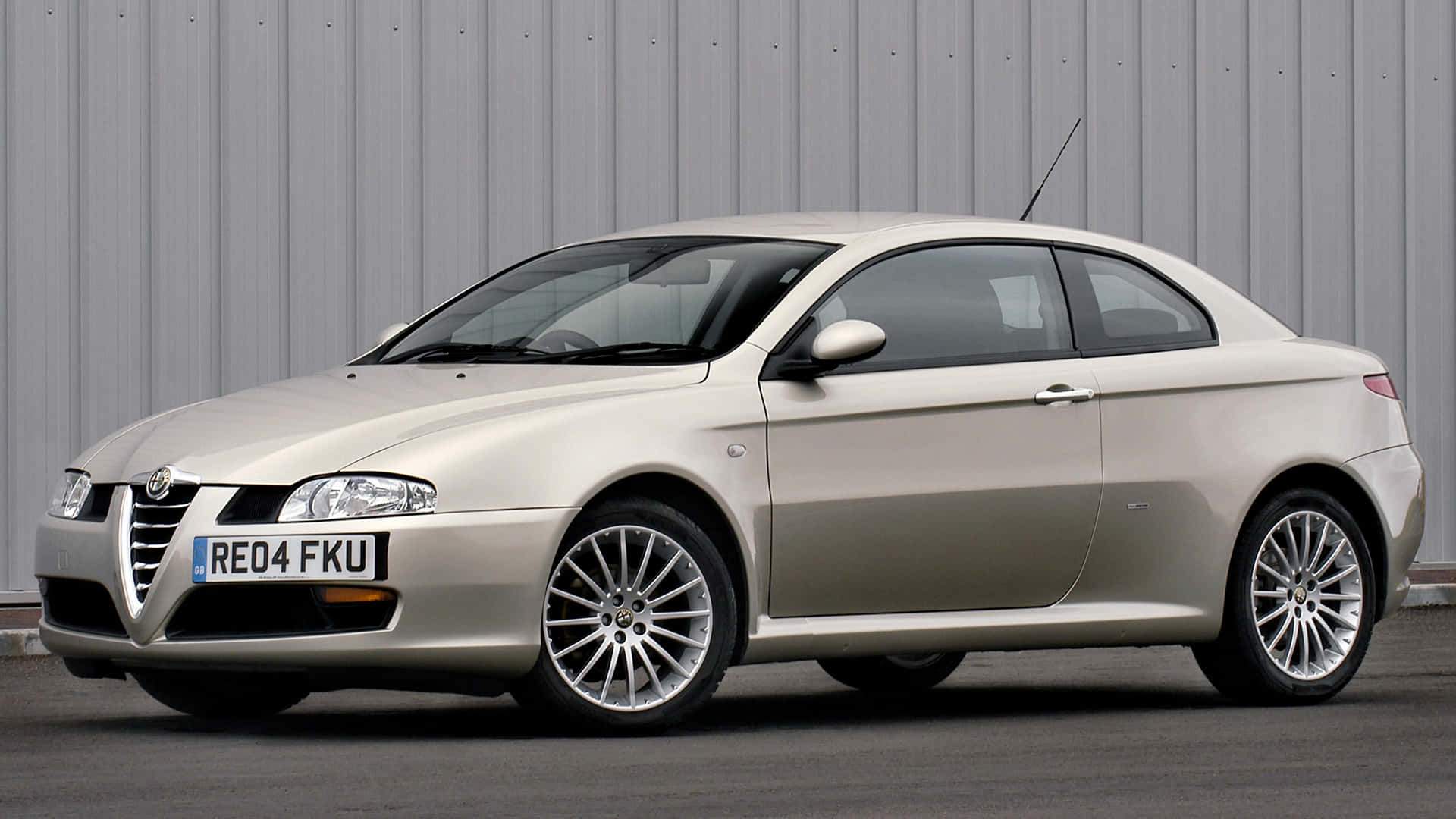 Alfa Romeo Gt 桌布 壁紙 — 一輛時尚的銀色愛快羅密歐雙門跑車停放在波紋金屬牆旁，配有拋光合金輪圈。