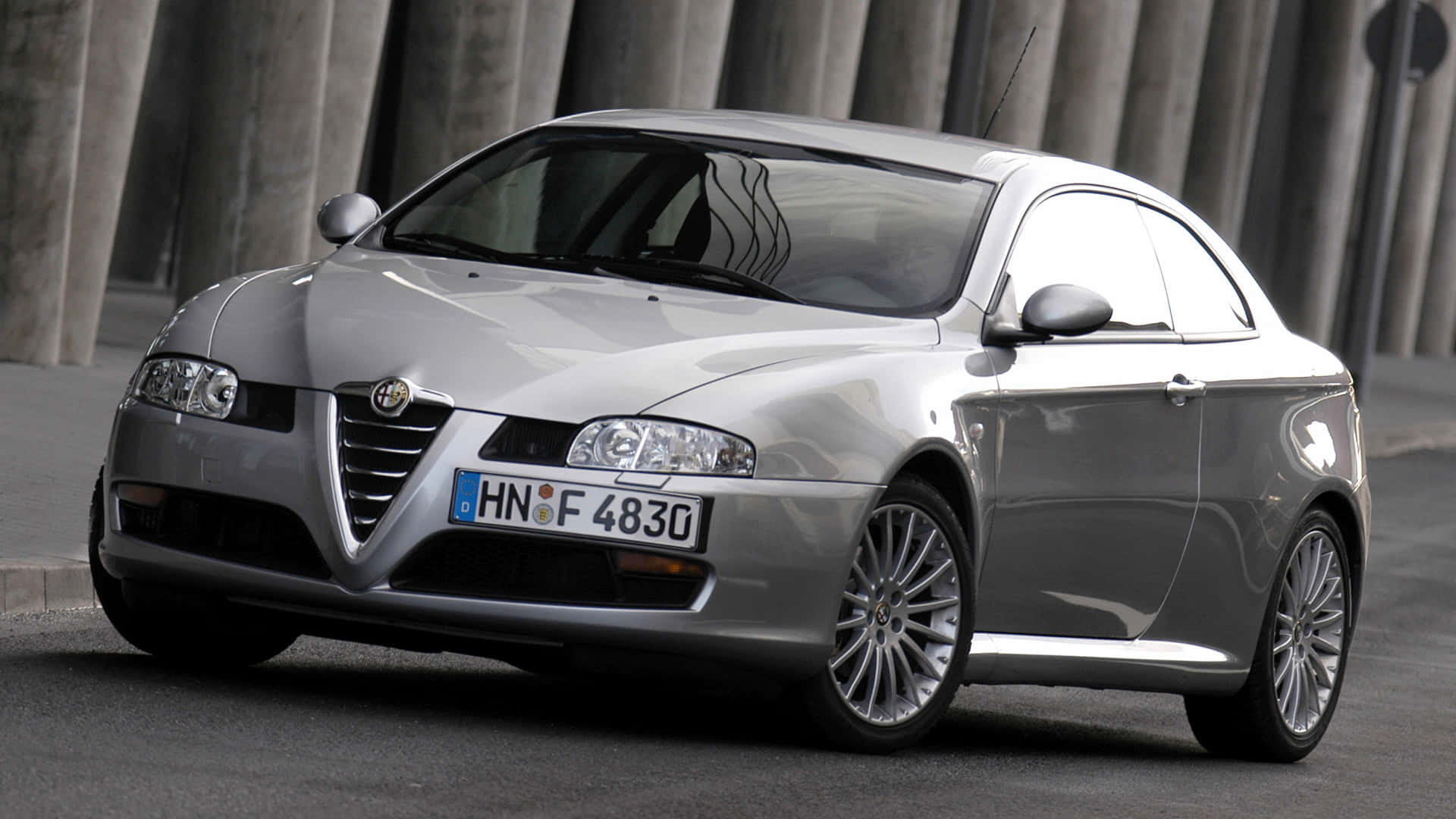 Alfa Romeo Gt 桌布 壁紙 — 一輛時尚的銀色愛快羅密歐雙門跑車停放在混凝土柱下，配備反光鍍鉻輪圈。