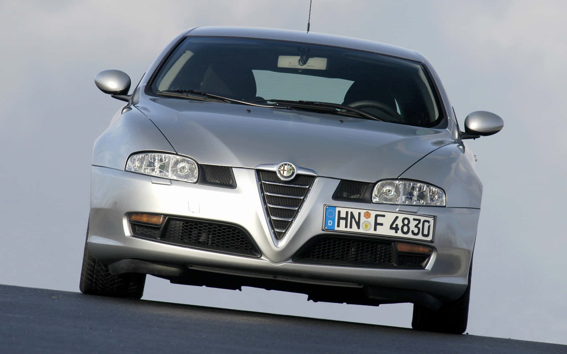 Alfa Romeo Gt 桌布 壁紙 — 一輛時尚的銀色愛快羅密歐跑車在陰天下朝前停在黑暗的道路上。