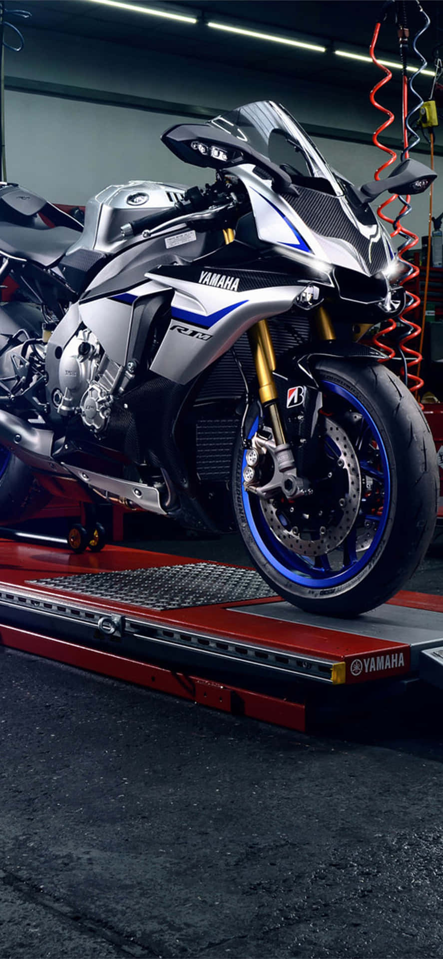  壁紙 — 一台流線型的銀藍色Yamaha R1機車在車庫明亮的燈光下，在紅色升降台上閃閃發光。