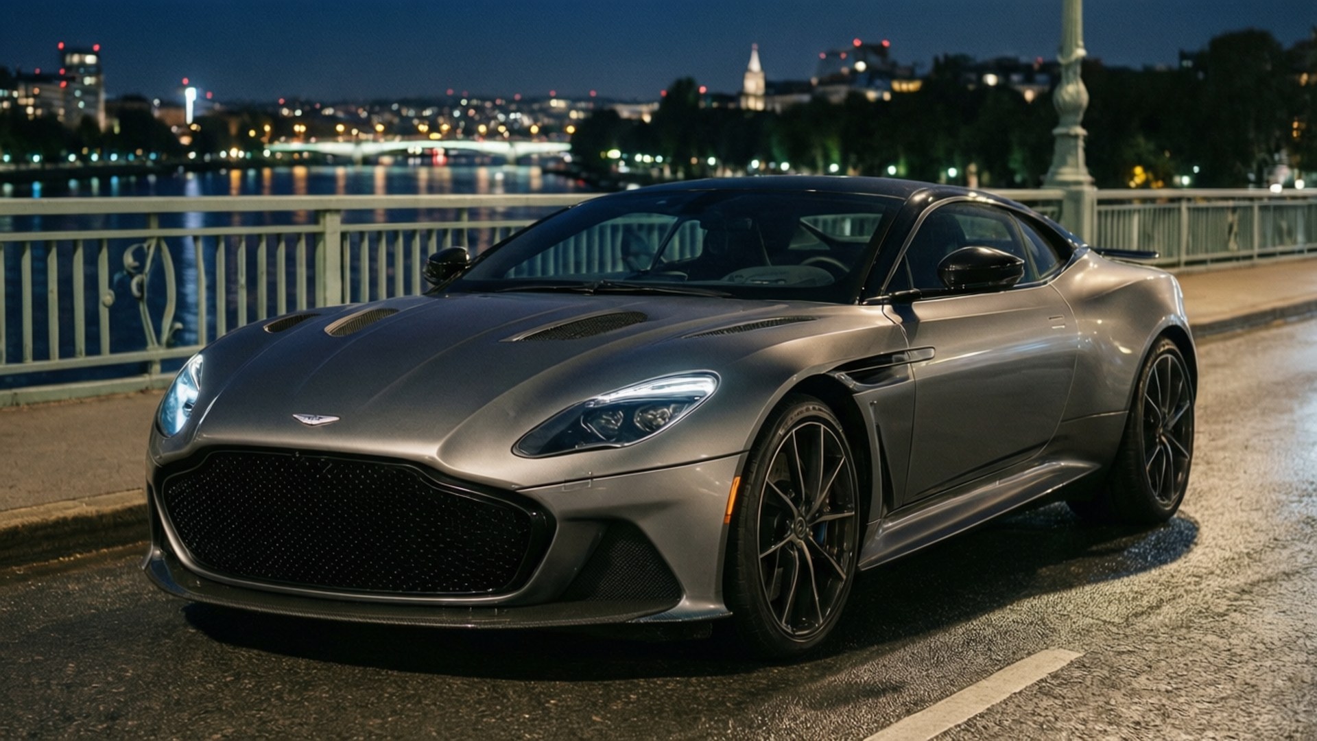Bridge of Elegance 壁紙 — 一架流線型銀色Aston Martin DB11停泊在濕滑的橋上，夜晚城市燈光倒映在後方的水面上。