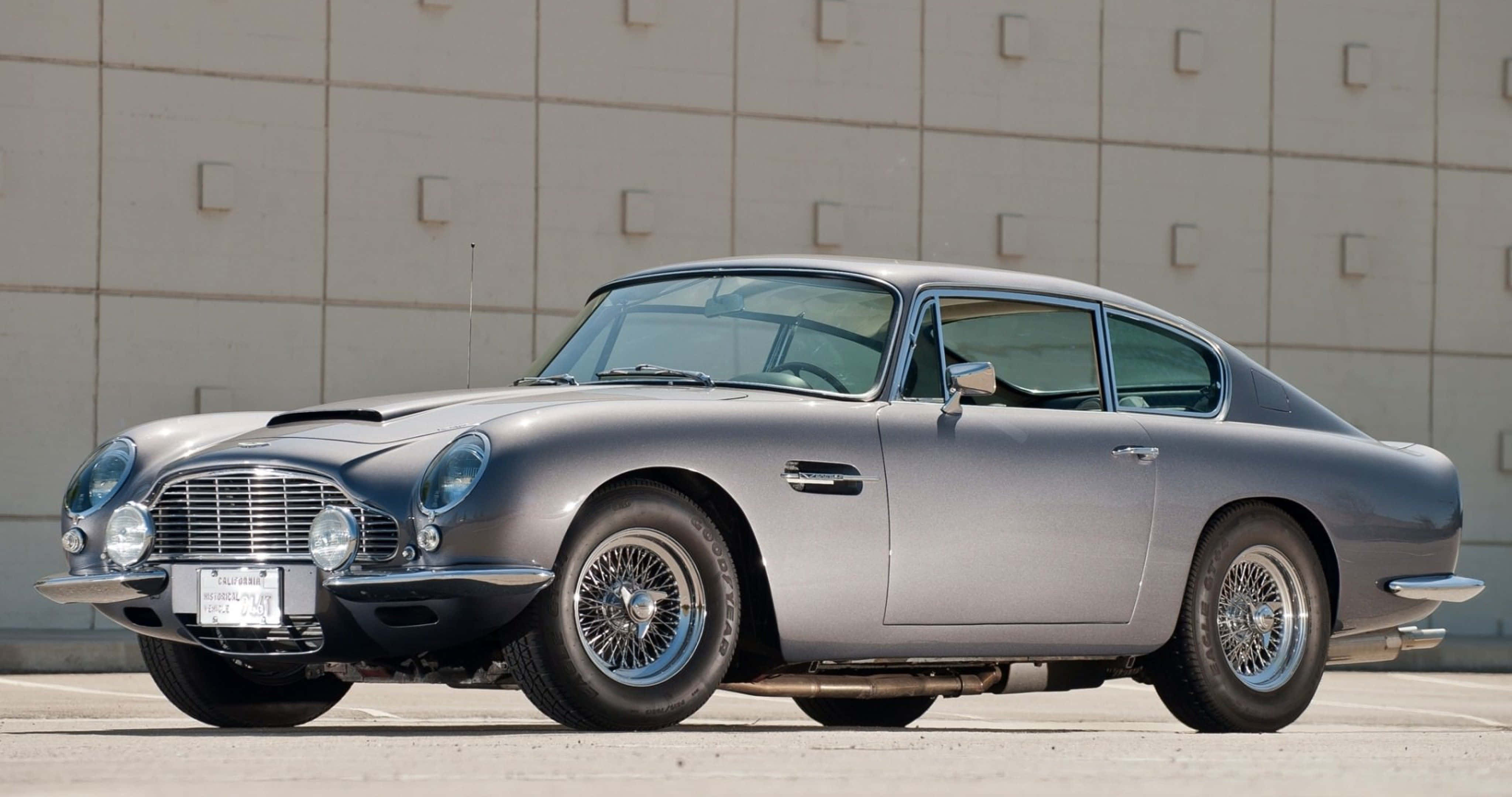 Aston Martin Db5 桌布 壁紙 — 一架流線型銀色Aston Martin DB5在明亮日光下閃耀，停在簡約混凝土牆前。