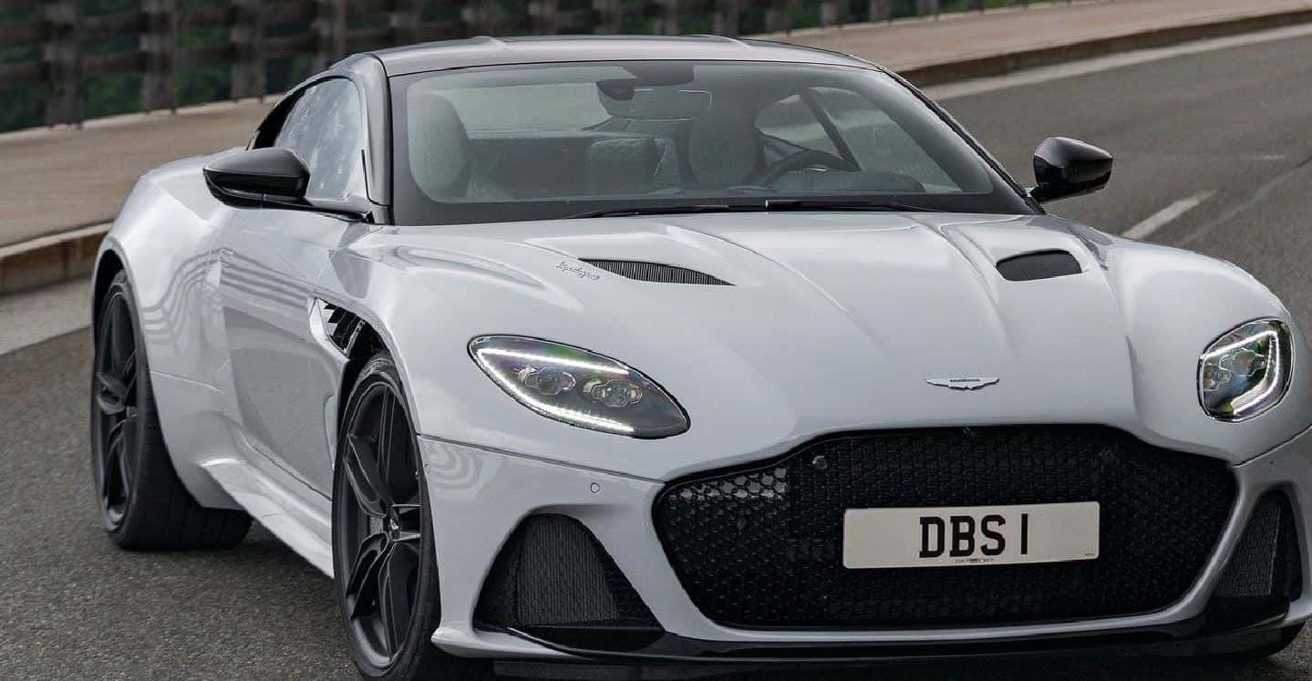 Aston Martin Dbs Superleggera 桌布 壁紙 — 一輛流線型銀色Aston Martin DBS1跑車沿著鋪砌道路行駛，配備黑色車輪和進取式前格柵。